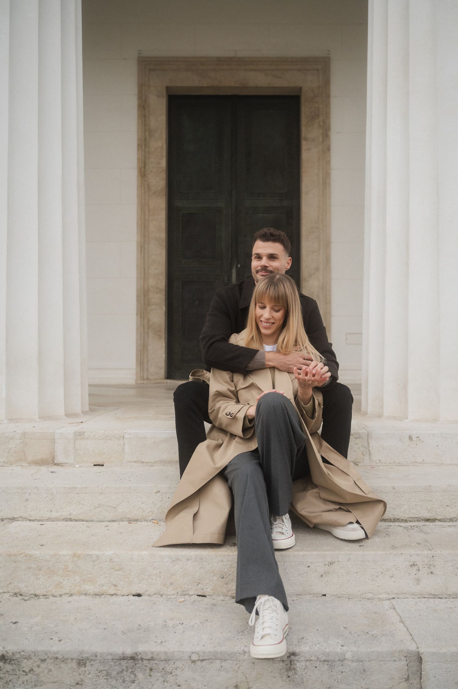 Person in beige coat and gray pants sitting on stone steps in a series of candid poses.