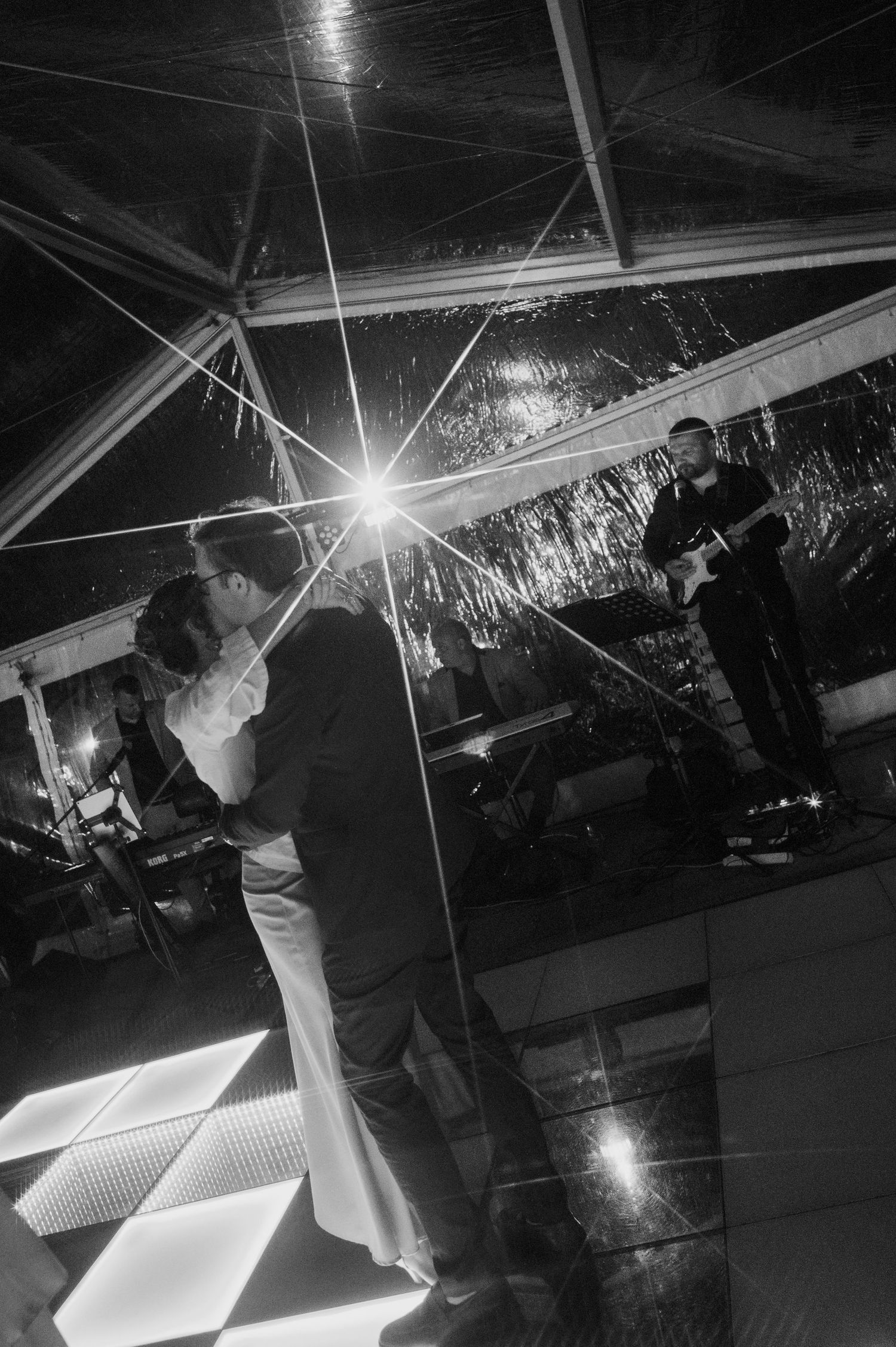 Black and white photo of a couple sharing a first dance with a live guitarist performing at their wedding.