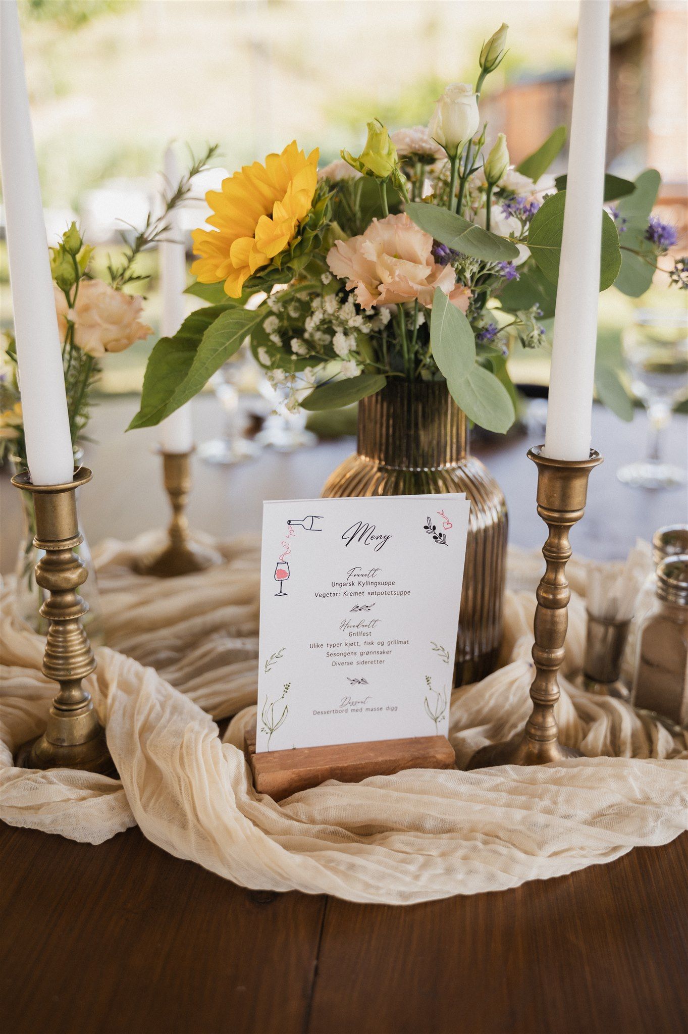 Elegant wedding table setting with white candles, menu cards, and yellow floral centerpieces.