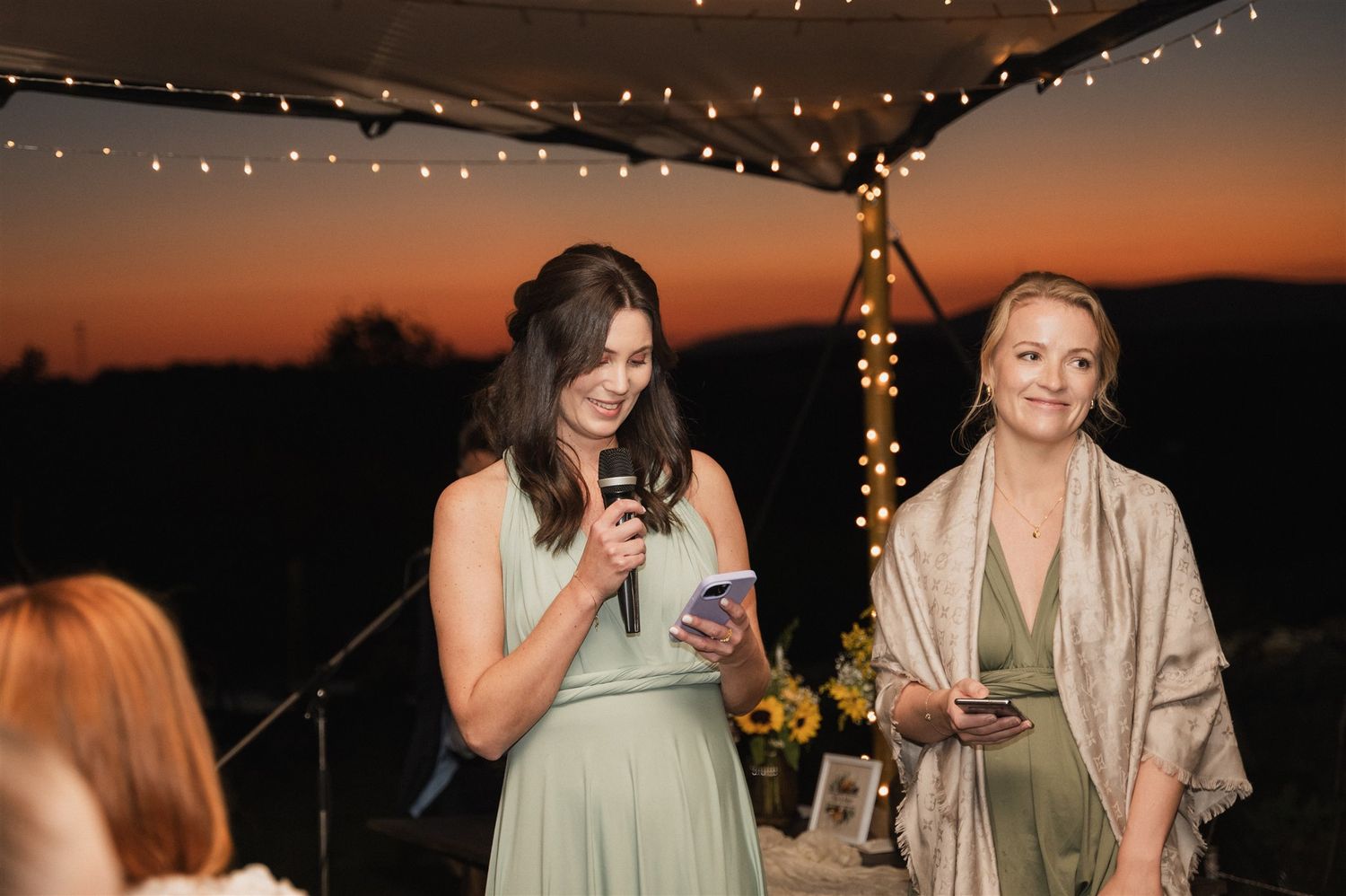 Evening wedding reception under string lights with guests mingling at sunset.