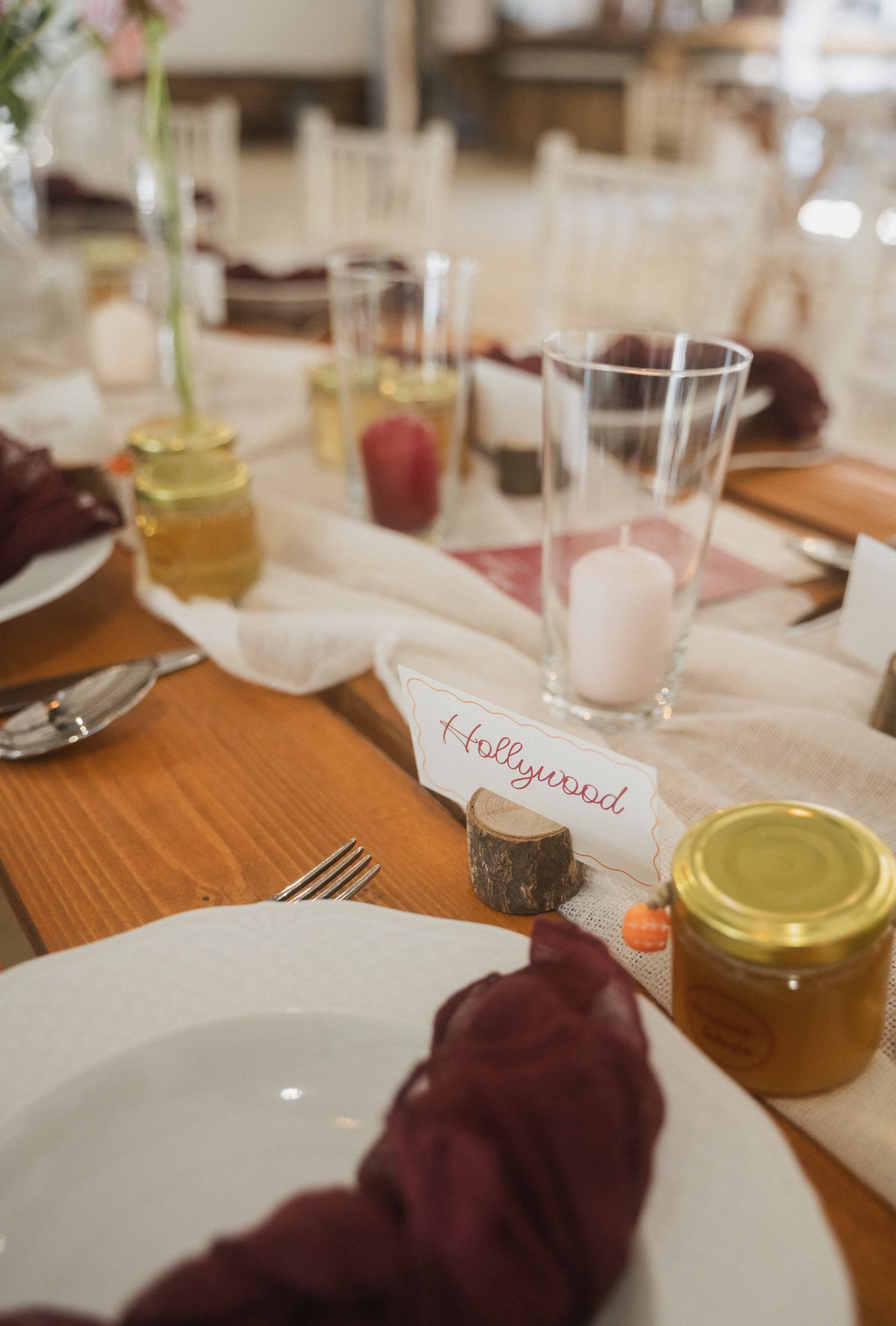 Place setting at an elegant dinner table with burgundy napkins, white plates, and honey jars on a wooden surface.
