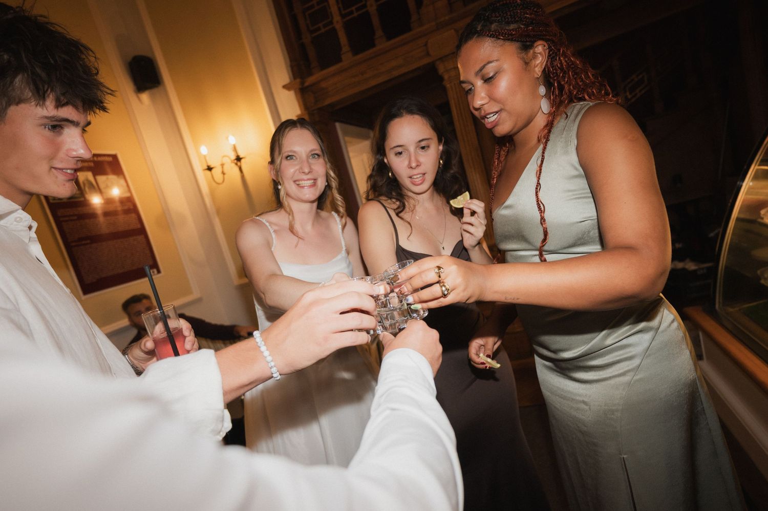 Bridesmaids and groomsman examining wedding jewelry under warm indoor lighting at reception.