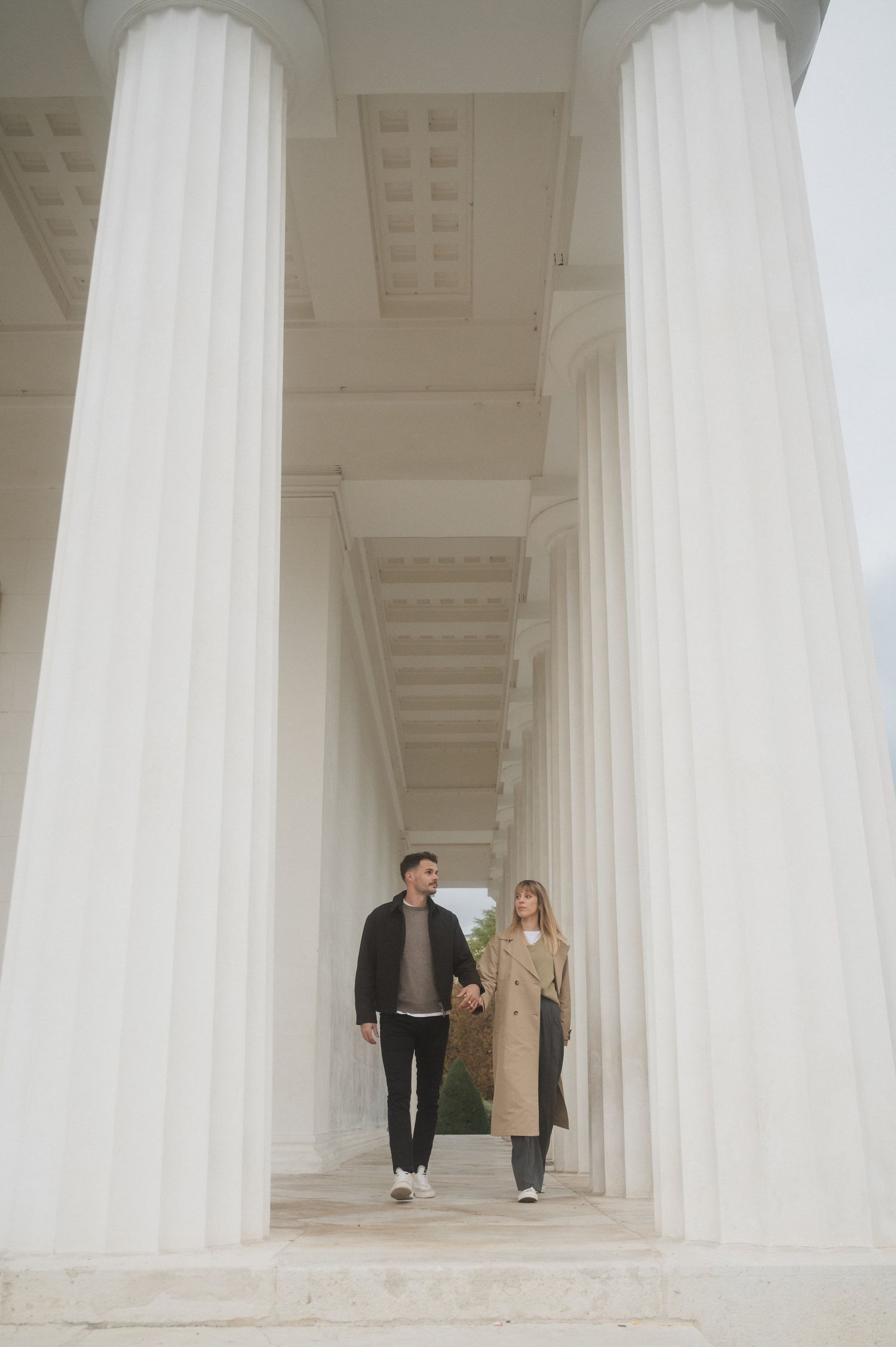 Two people walking through a modern white colonnade with dramatic architectural columns and shadows.