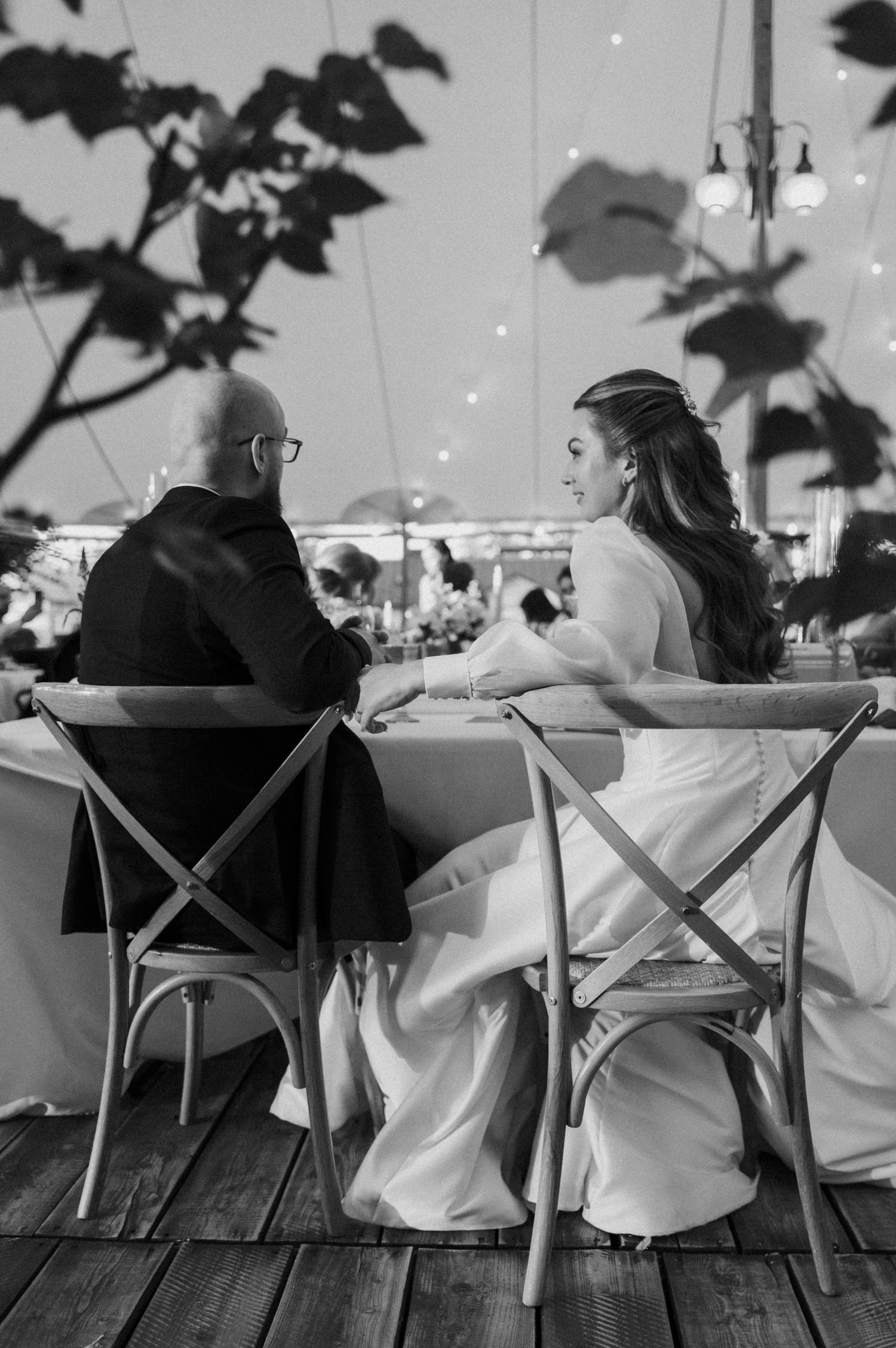 A black and white panoramic sequence of people sitting at tables on a wooden deck in a casual outdoor setting.