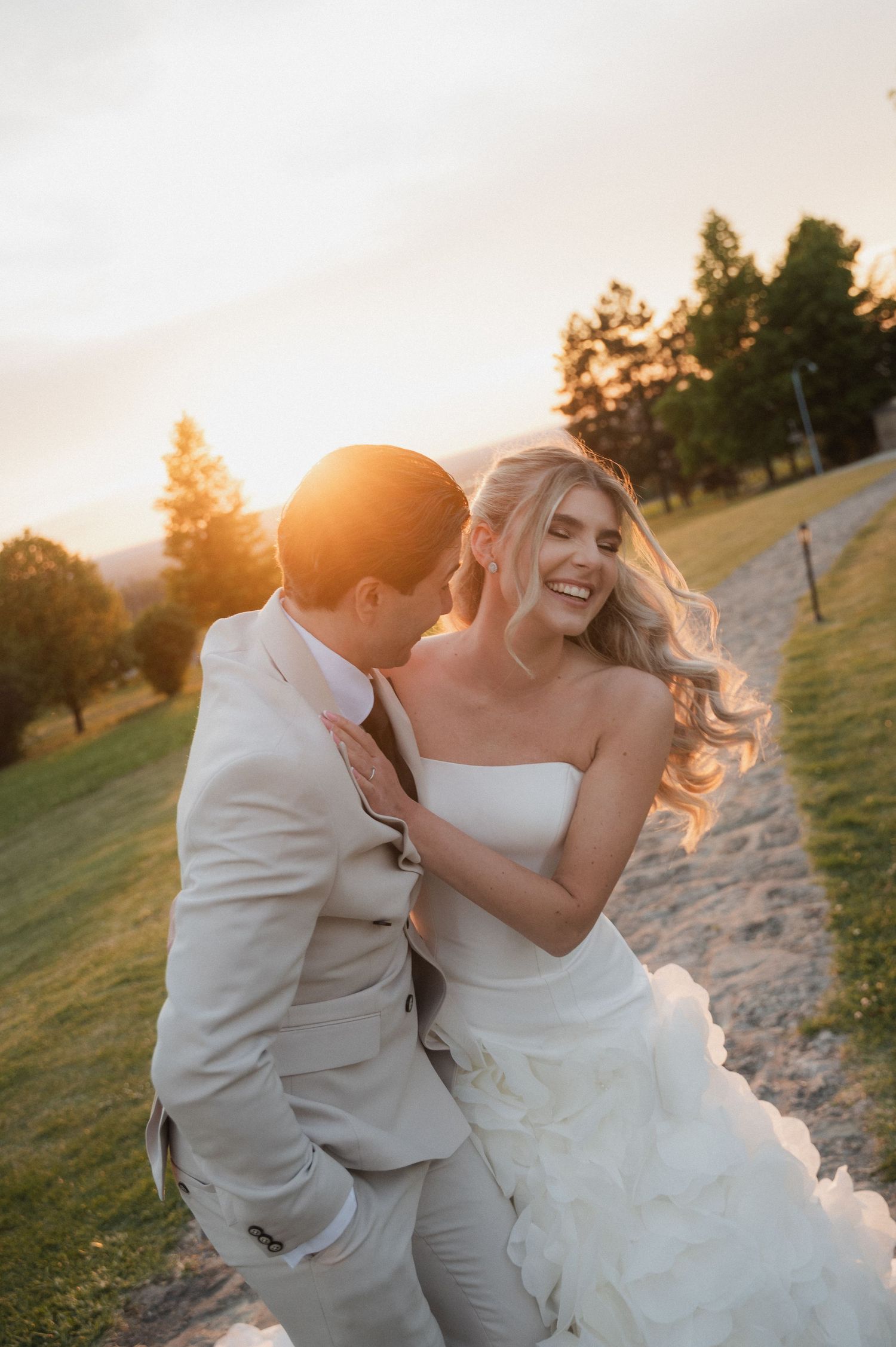 Romantic golden hour portrait of bride and groom embracing on a sunlit outdoor wedding venue path.