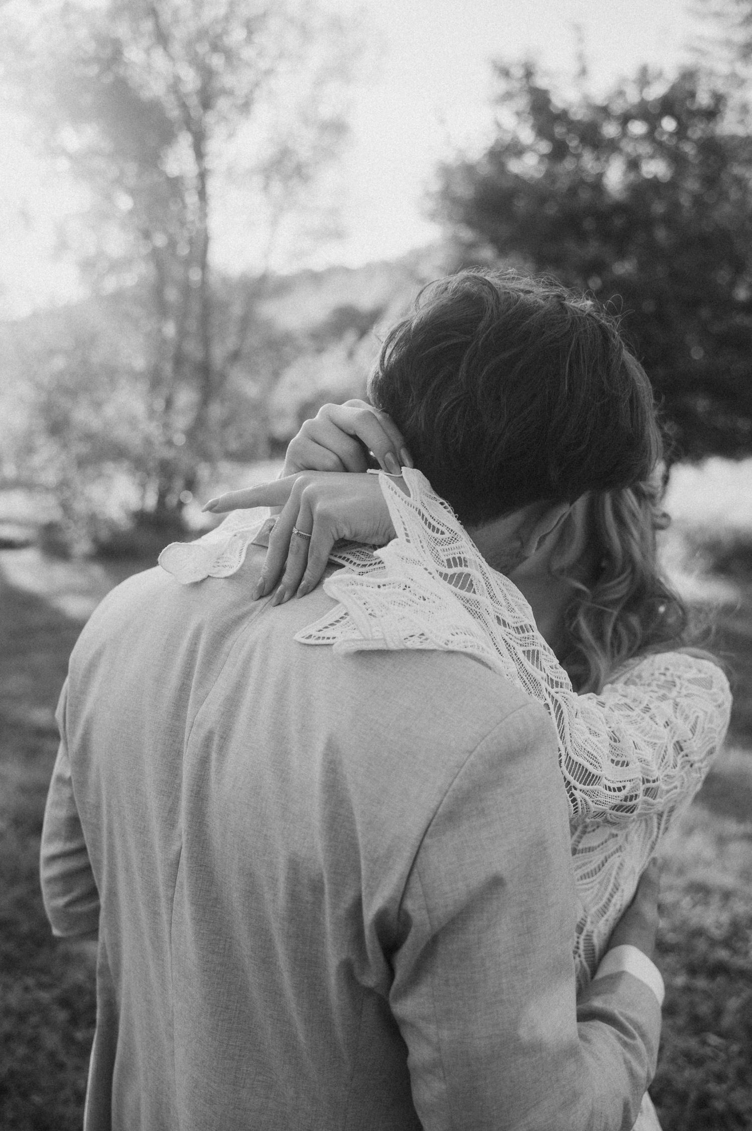 A tender black and white photograph showing an intimate embrace between two people outdoors in nature.