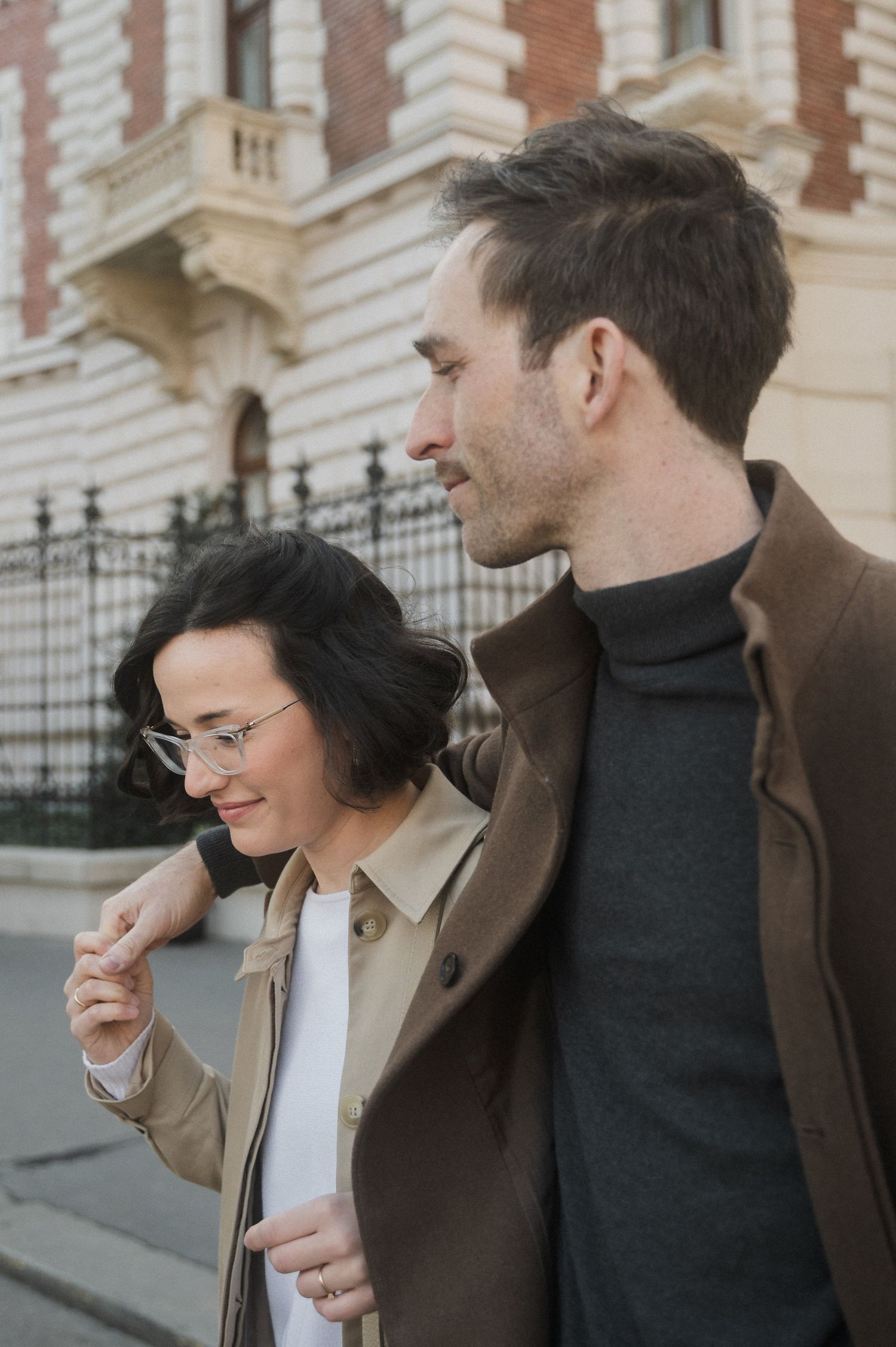 Two people in business attire share a candid laughing moment together outside a building with ornate architecture.