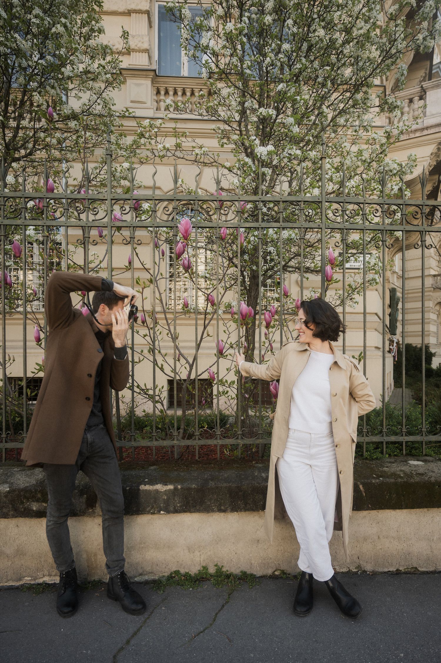A series of five images showing two people in contrasting outfits interacting near a garden wall with trees.