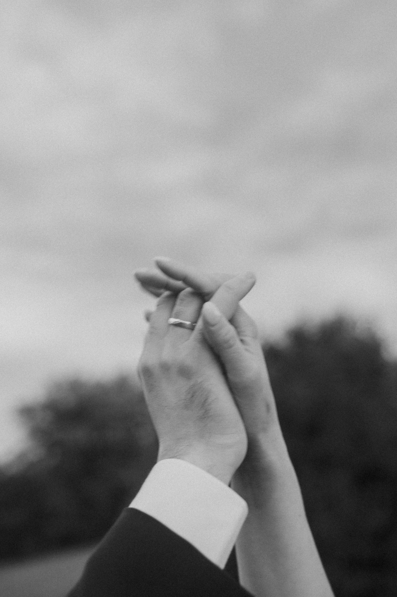 Close-up of intertwined hands against a blurred natural background in black and white.