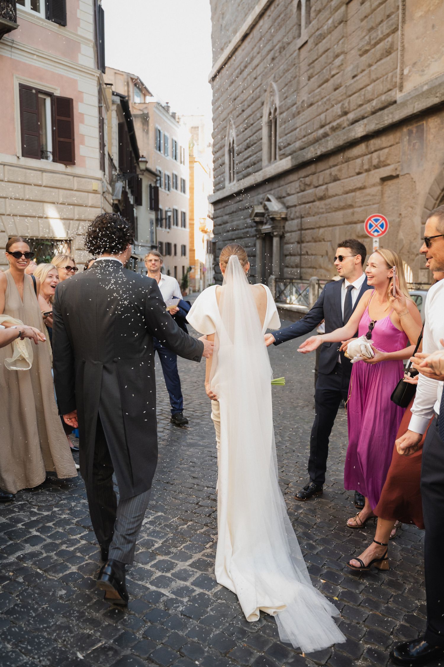 Wedding celebration on cobblestone street with guests throwing confetti.