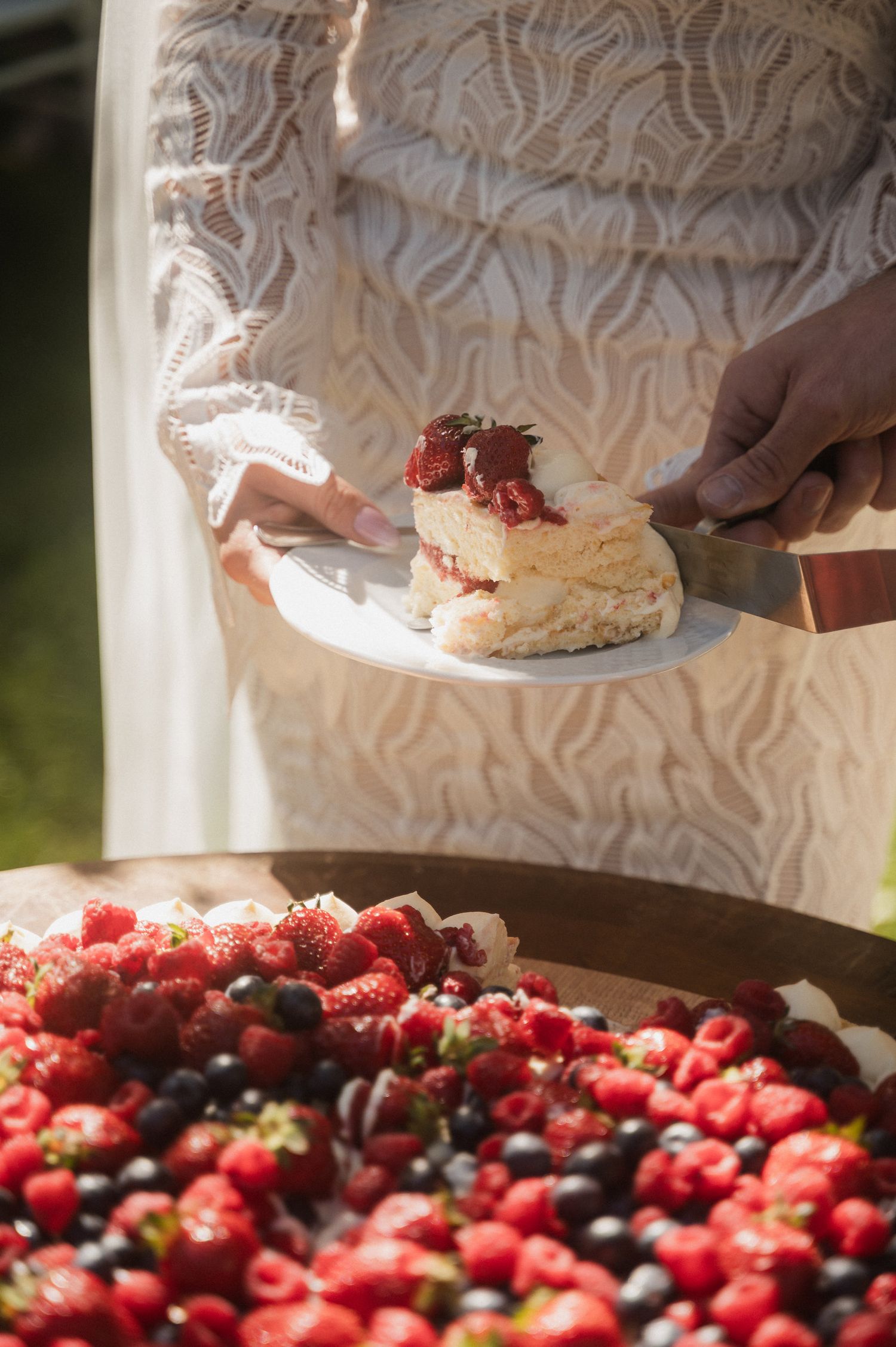 Hands assembling a berry shortcake dessert with fresh strawberries and blueberries on a white plate.