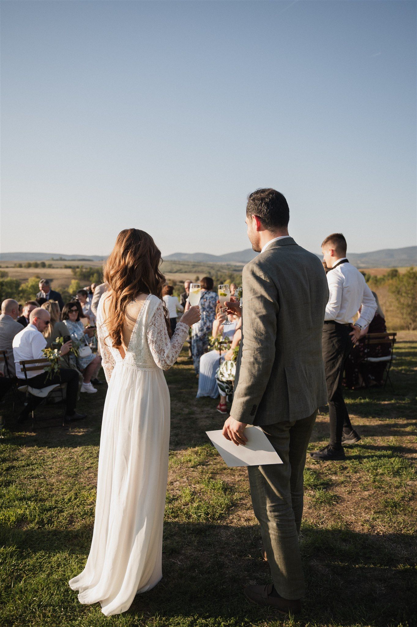Wedding ceremony guests gather outdoors in a scenic mountain landscape during golden hour.