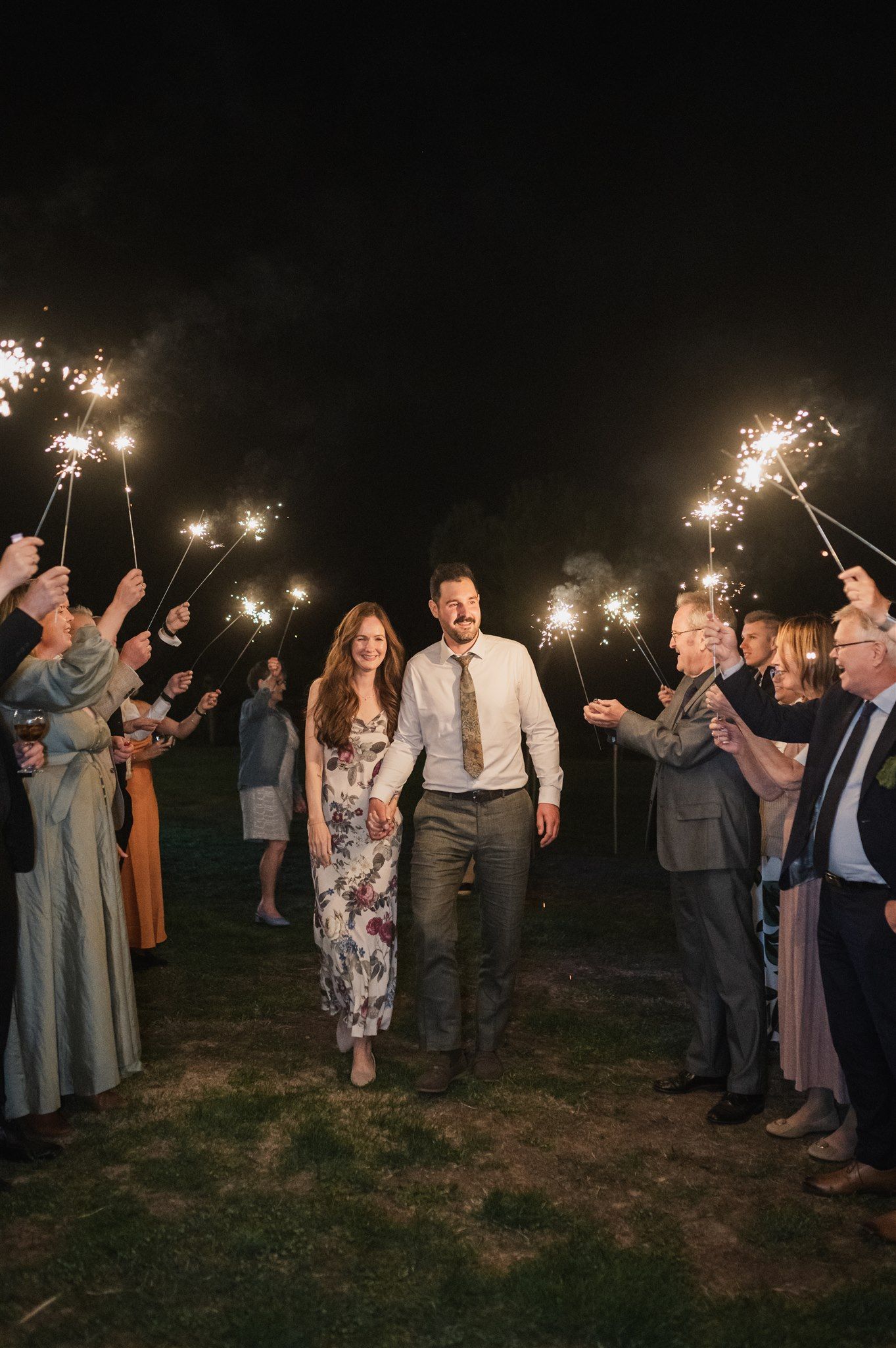 Wedding guests hold sparklers during an evening celebration outdoors.