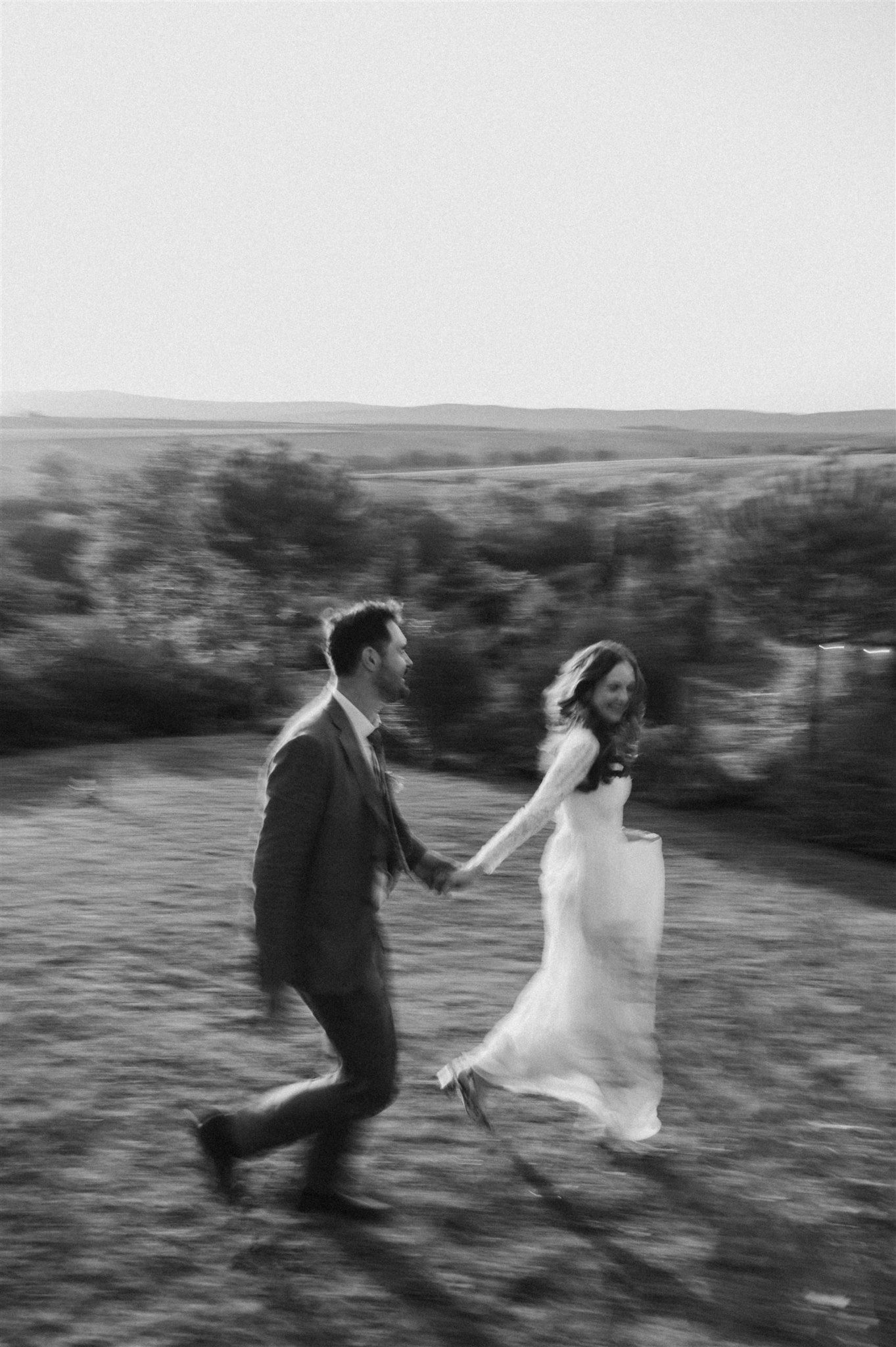 Black and white photo of a couple running through a field, their movement creating a blurred effect.
