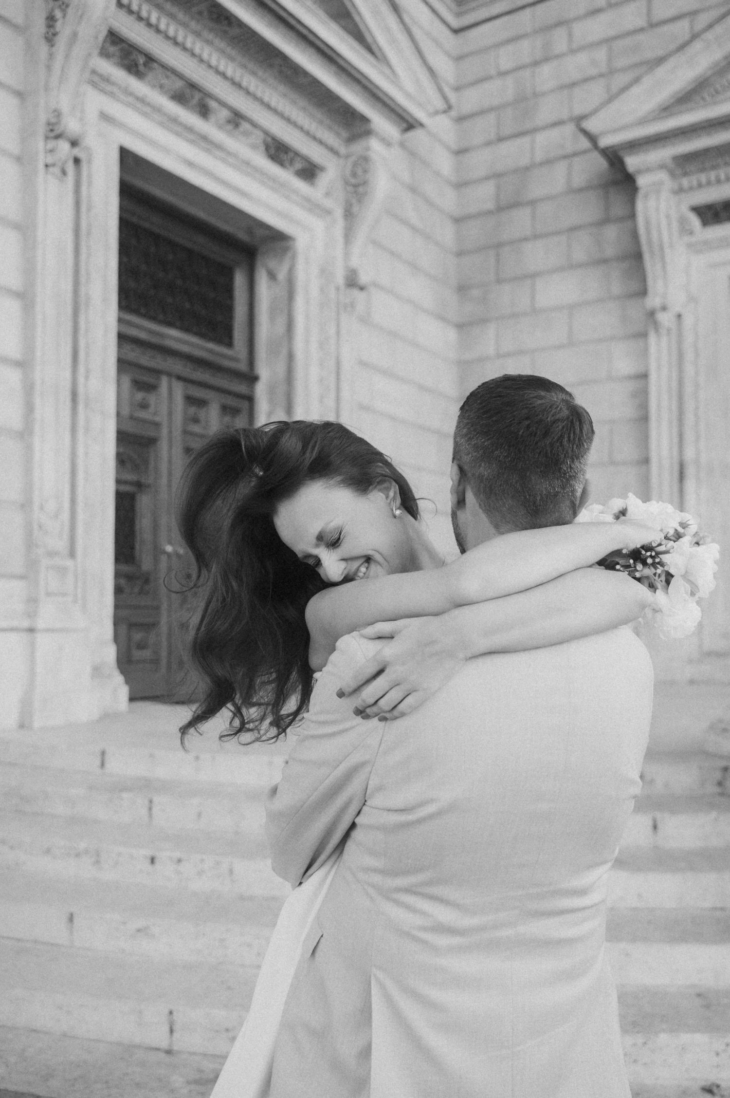 Wedding couple embraces in romantic dance pose by classical architecture.