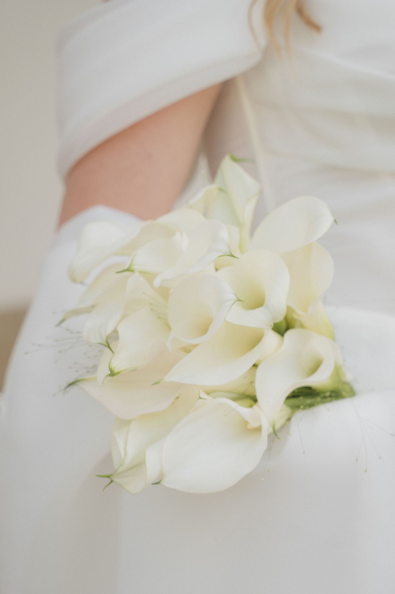 Bride holding a elegant wedding bouquet of white calla lilies in her white off-shoulder bridal gown.