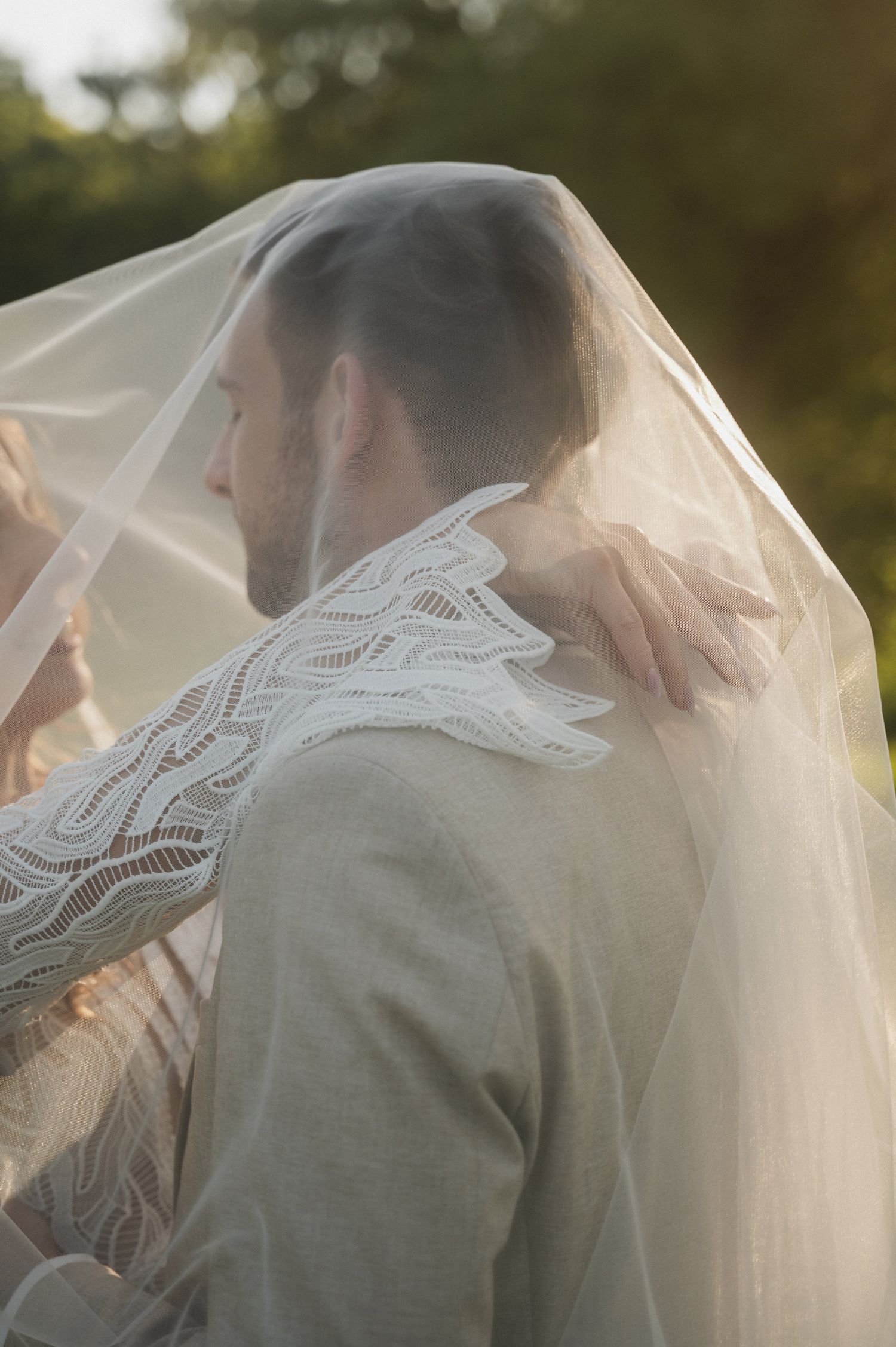 A romantic wedding moment captured through a delicate lace veil in soft natural lighting.