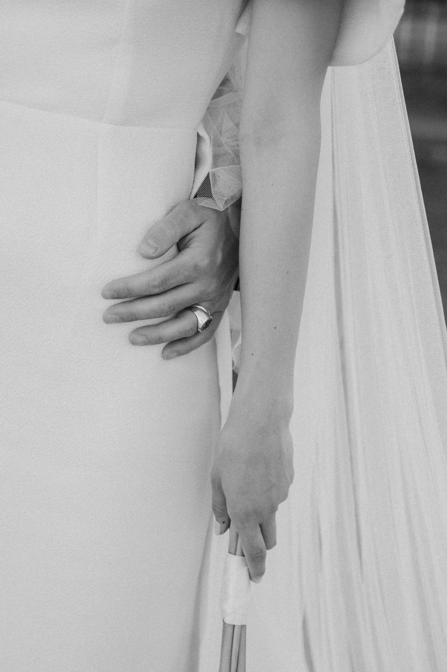 Close-up details of hands and flowing white wedding dress fabric.