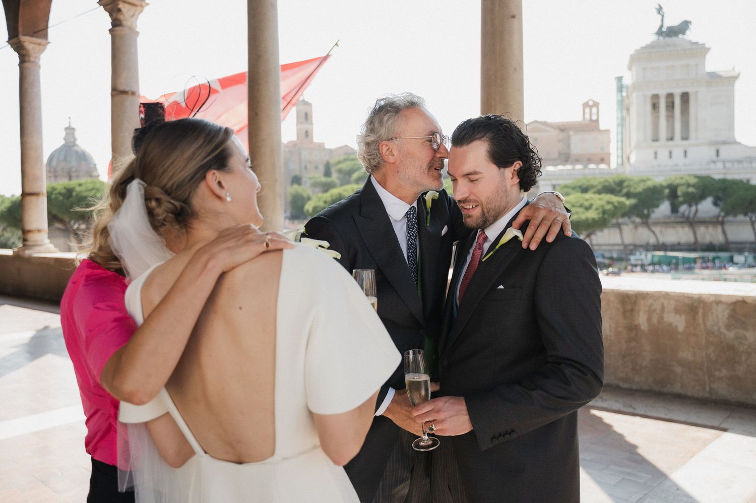 Wedding guests socialize and toast during an outdoor reception under stone archways.