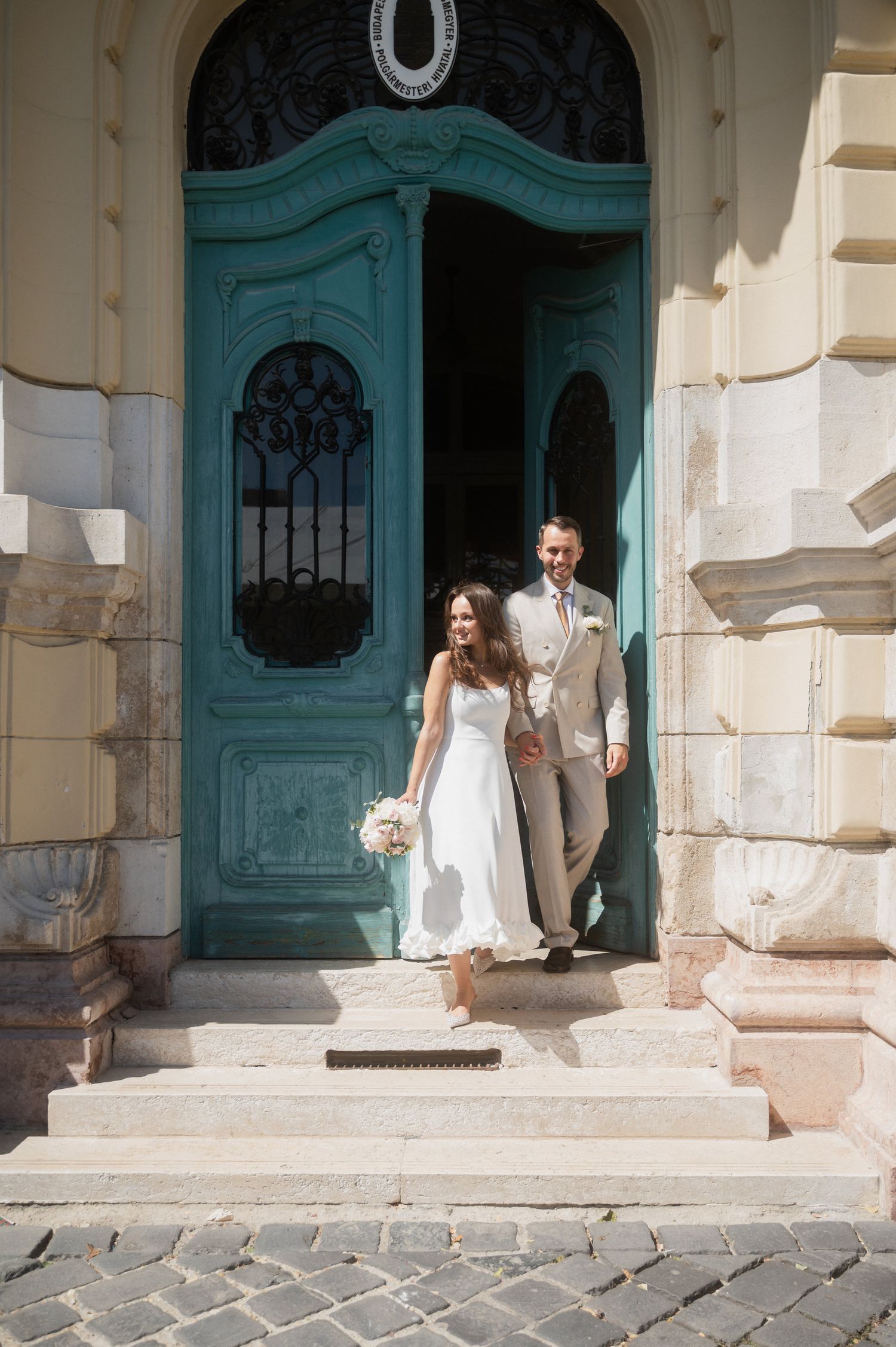 Wedding couple poses on stone steps in front of a turquoise vintage door.