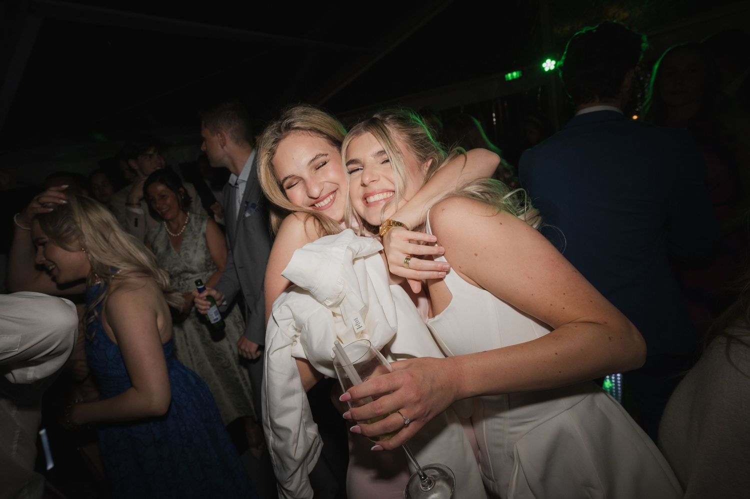 Two smiling women hugging and celebrating together at a lively wedding reception party.