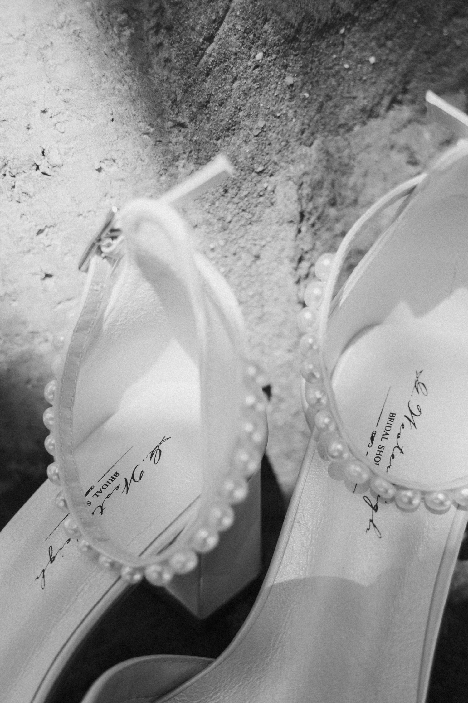 Close-up black and white photo of pearl-adorned bridal heels with delicate ankle straps for a wedding.