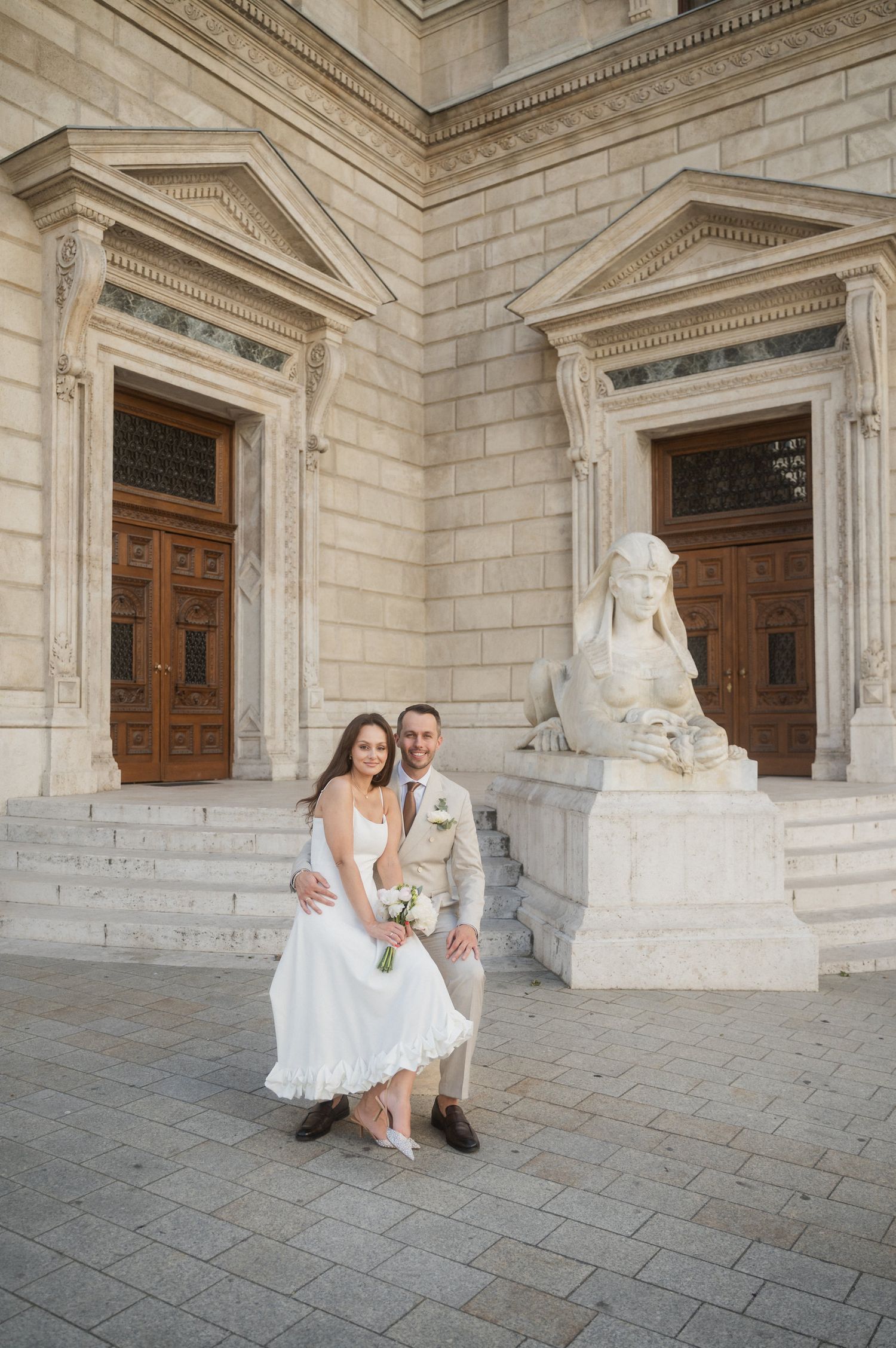 Wedding couple poses on stone steps of grand historic building with wooden doors.