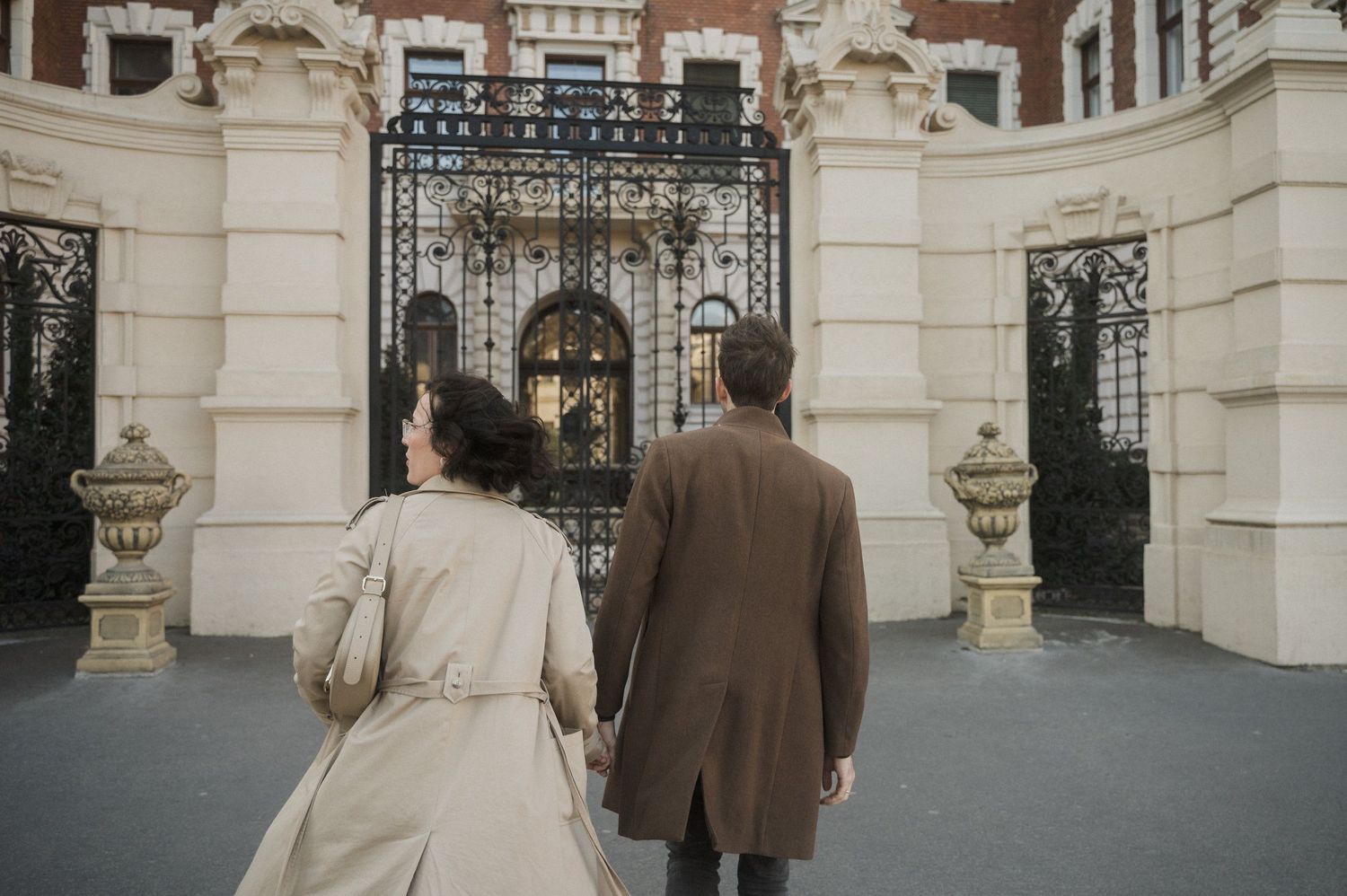 A couple walks toward an ornate white stone gate entrance with decorative architectural details.