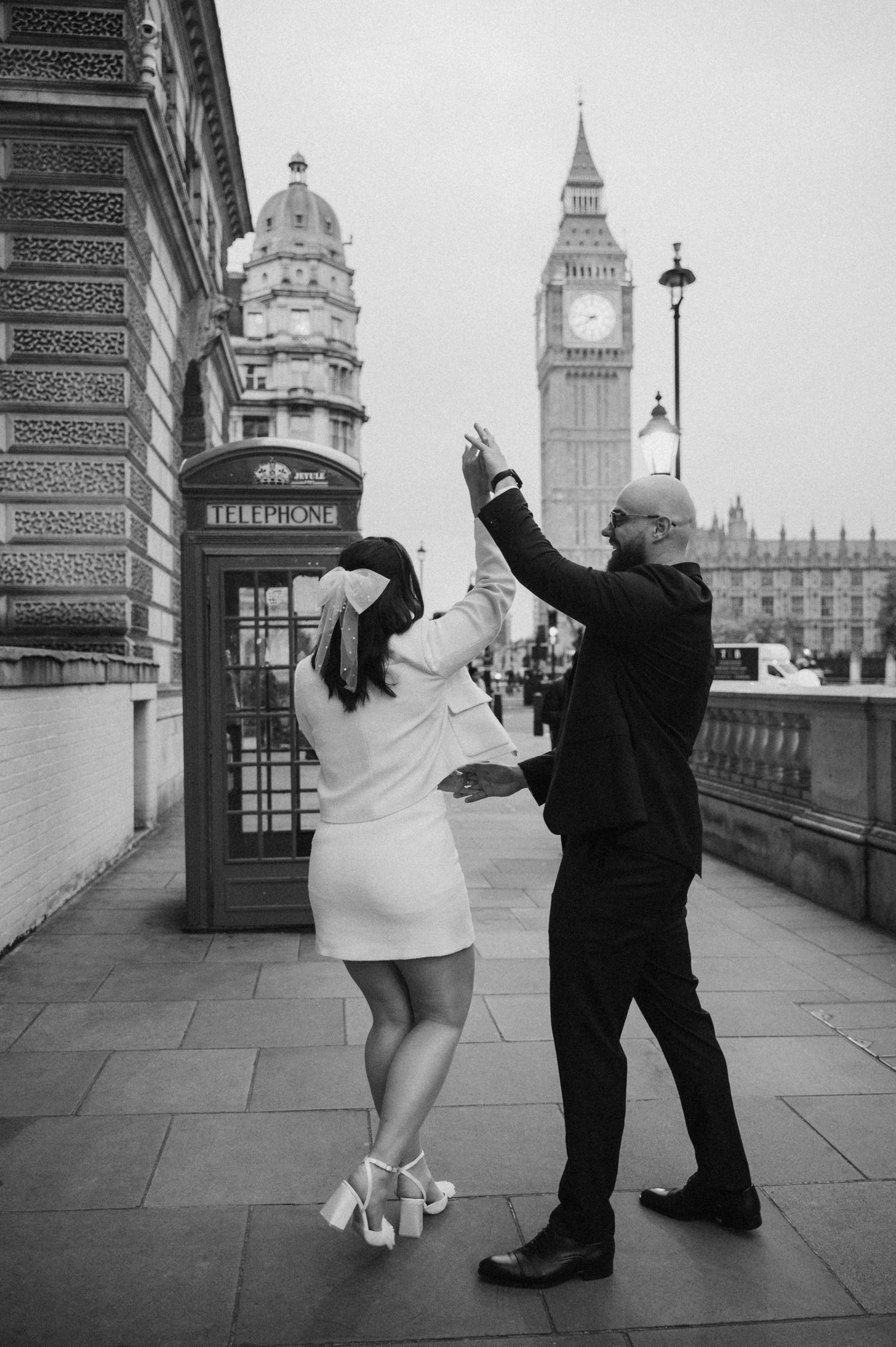 A couple dances playfully by a London phone booth with Big Ben in view.