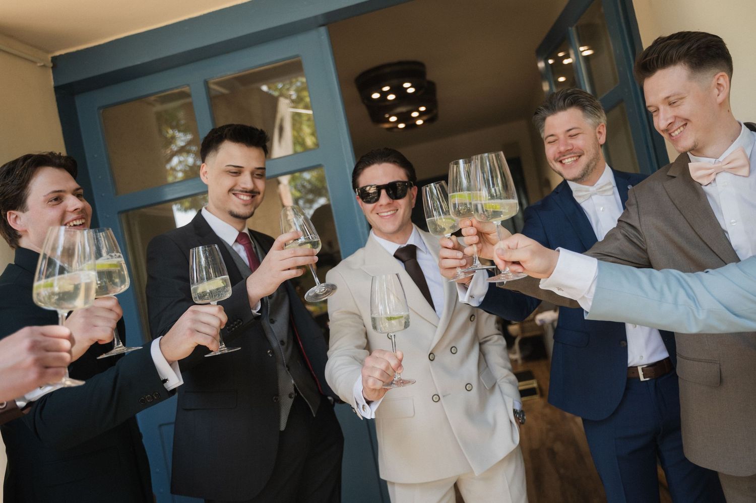 Groom and groomsmen in suits toasting with champagne glasses before the wedding celebration.