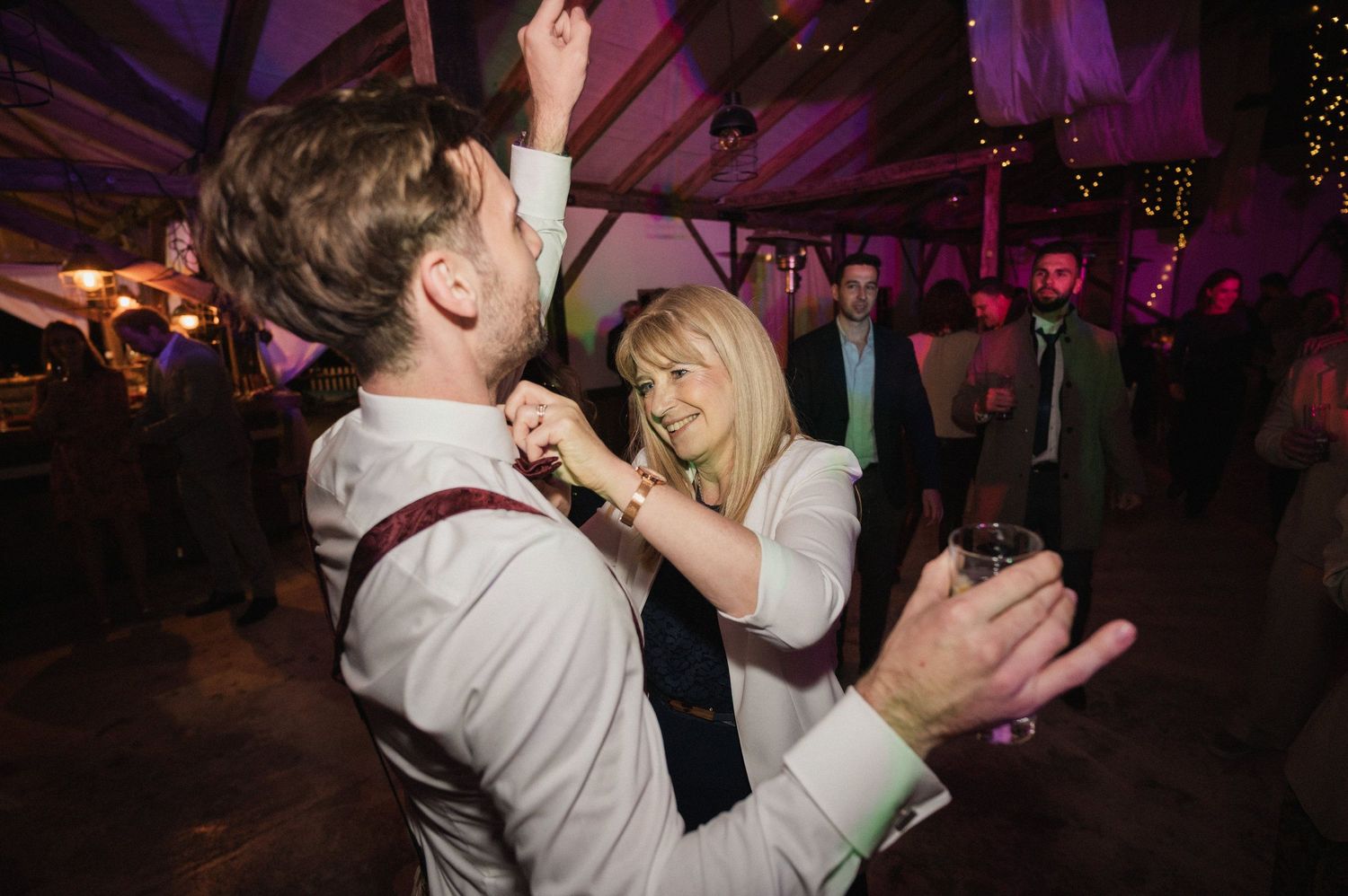A couple dances together at a wedding reception under purple lighting in a decorated tent venue.