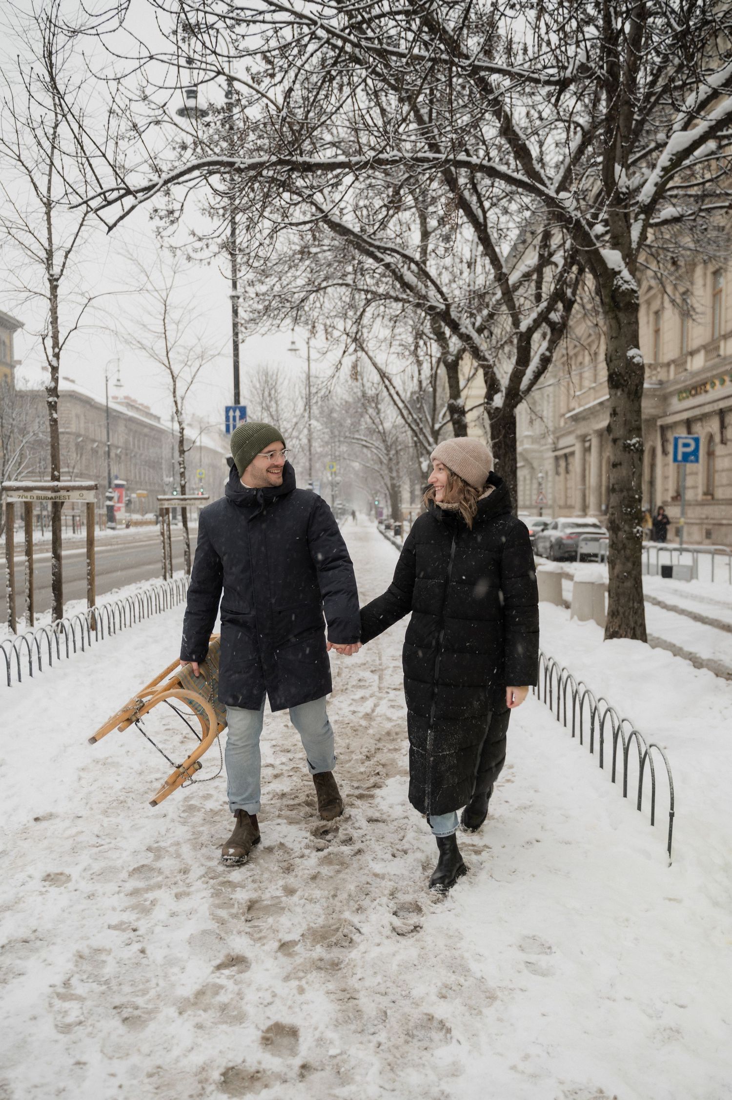 Two people walking together through a snowy tree-lined path in winter.