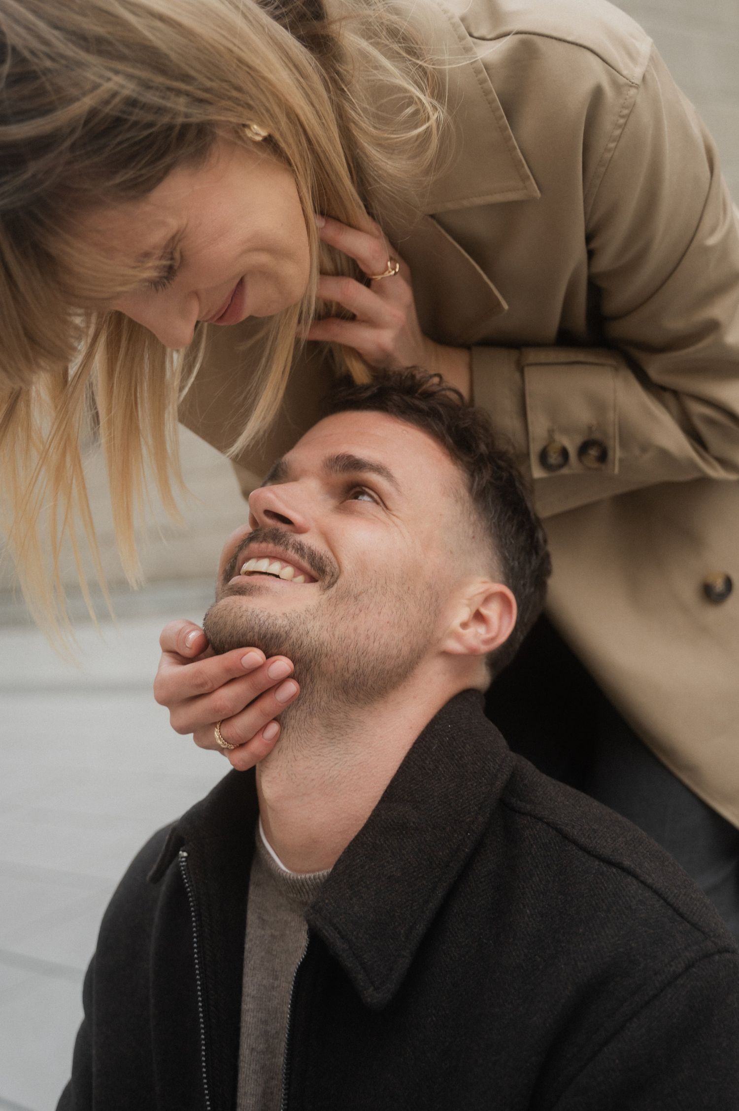 A playful couple shares an intimate moment as they laugh and embrace while wearing neutral-toned clothing.