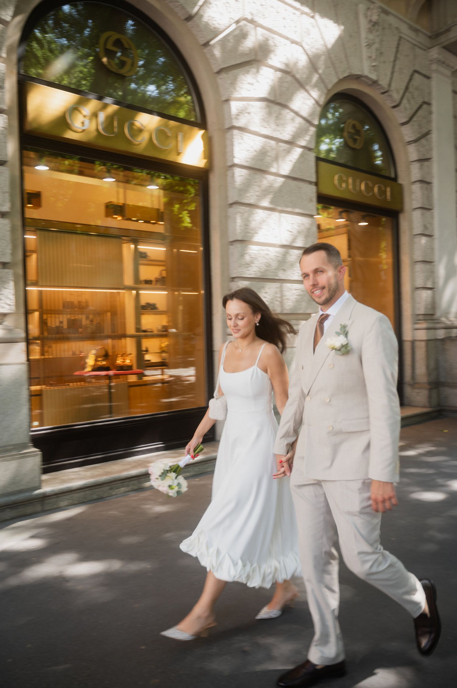 Dancing couple in white attire moves gracefully past luxury storefronts with arched architecture.