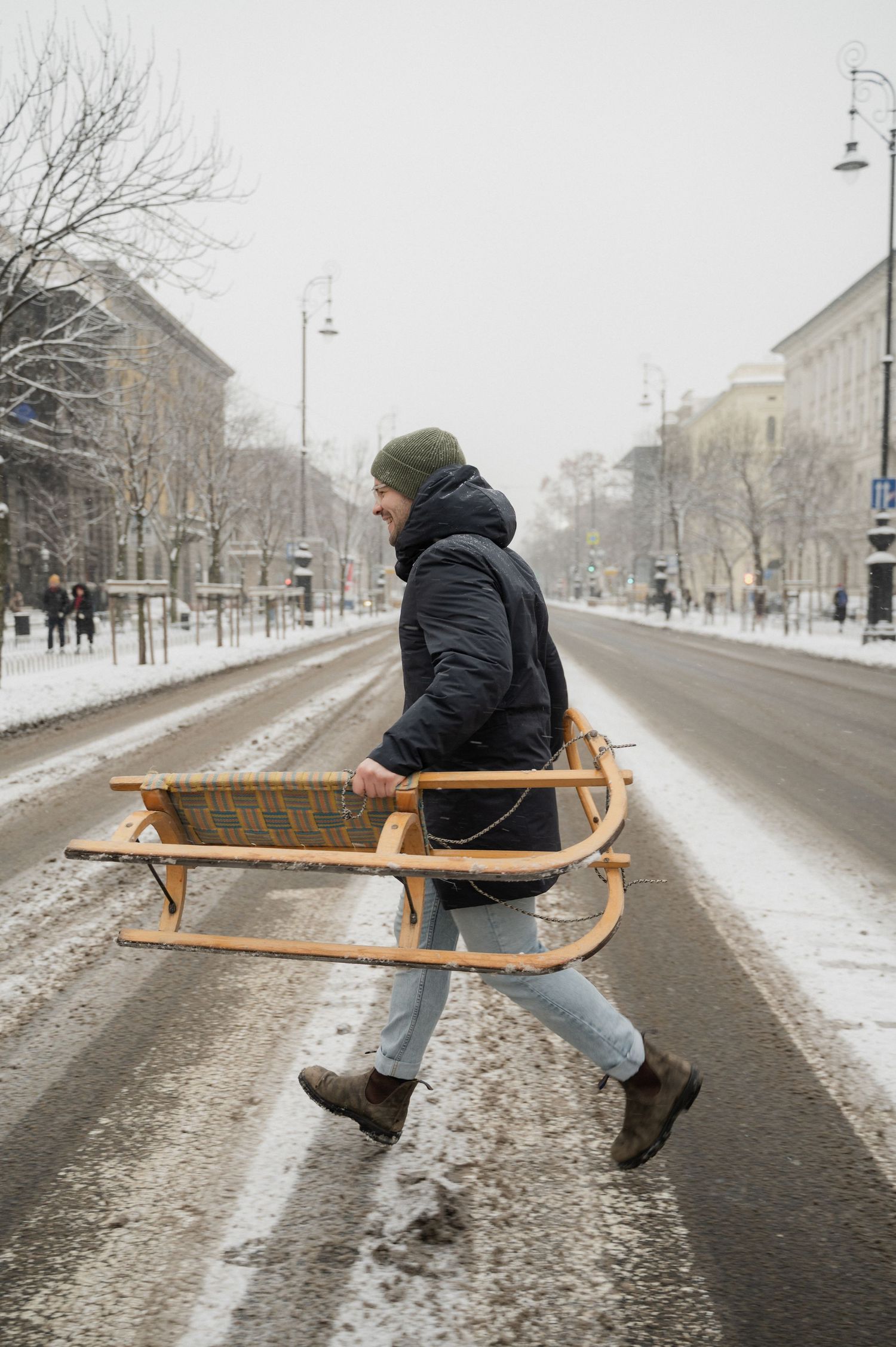 Someone riding a wooden sled down a snowy urban street.