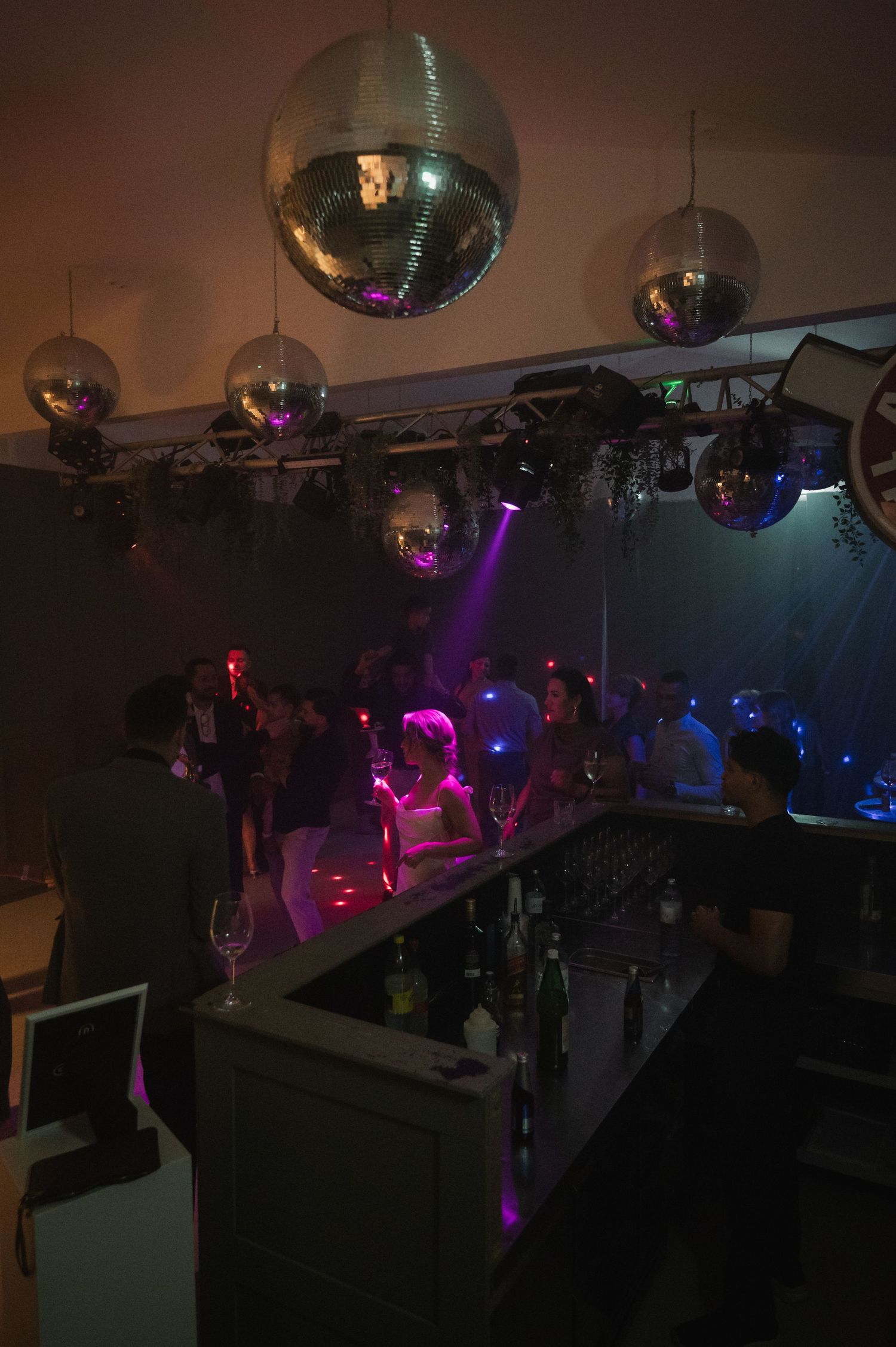 Wedding reception dance floor with disco mirror balls, colorful lights, and guests celebrating at the bar.