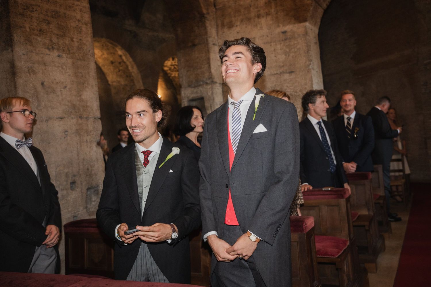 Wedding guests mingling in formal attire inside historic brick building.