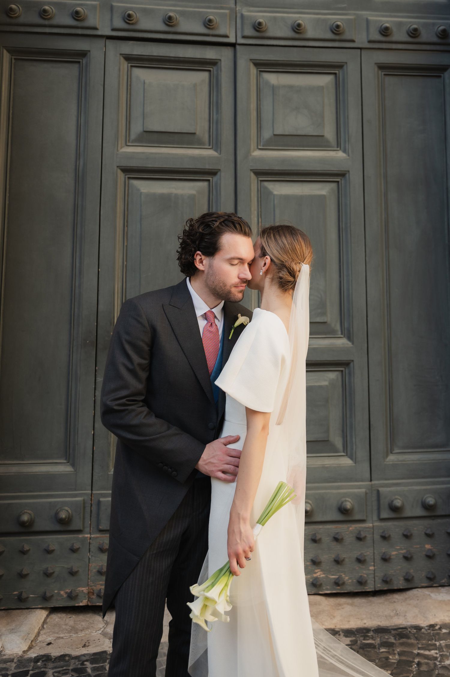 Romantic wedding portrait against large wooden doors with decorative metal studs.