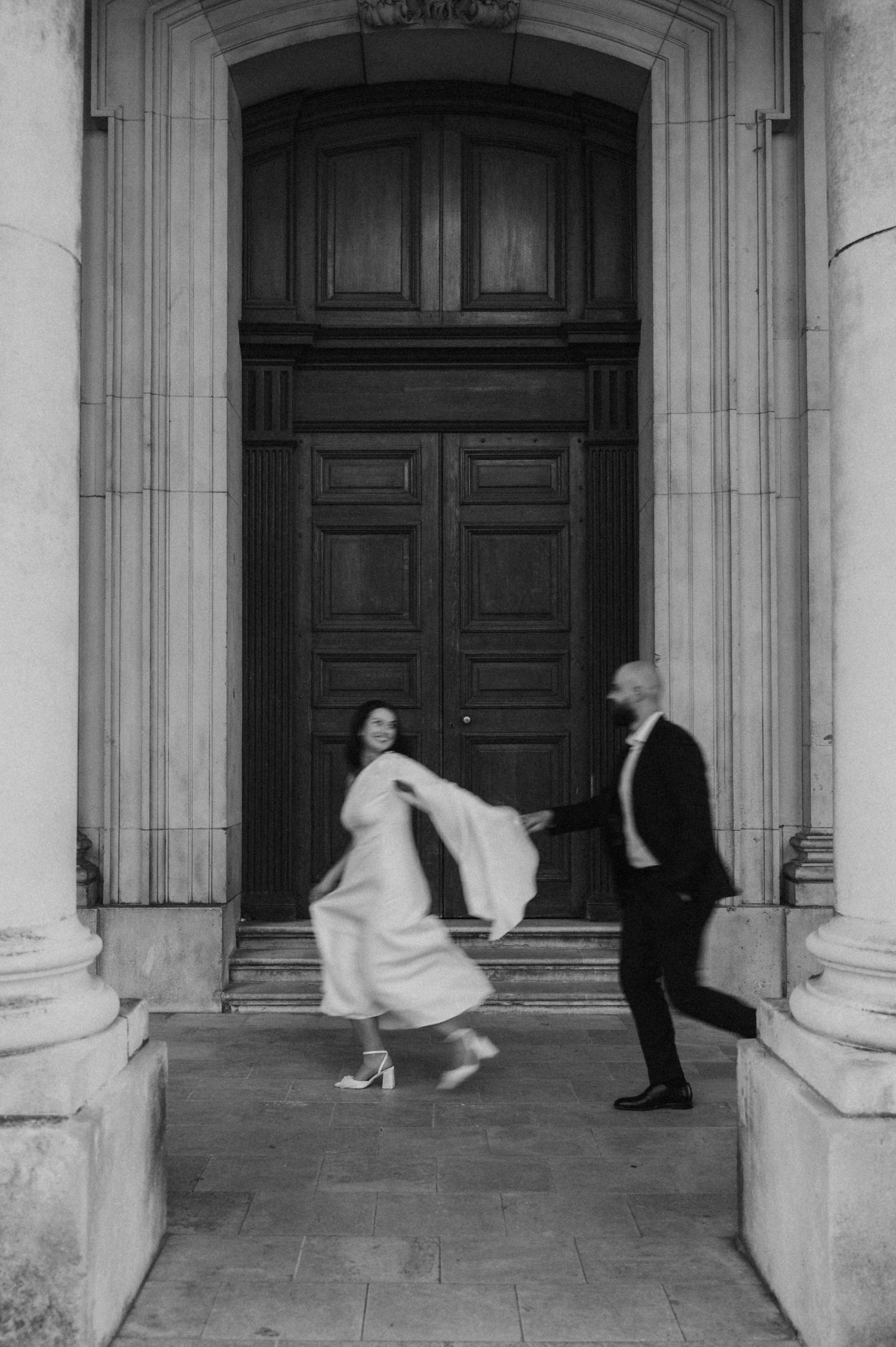 Black and white sequence capturing flowing movement of bride's dress against classical columns.