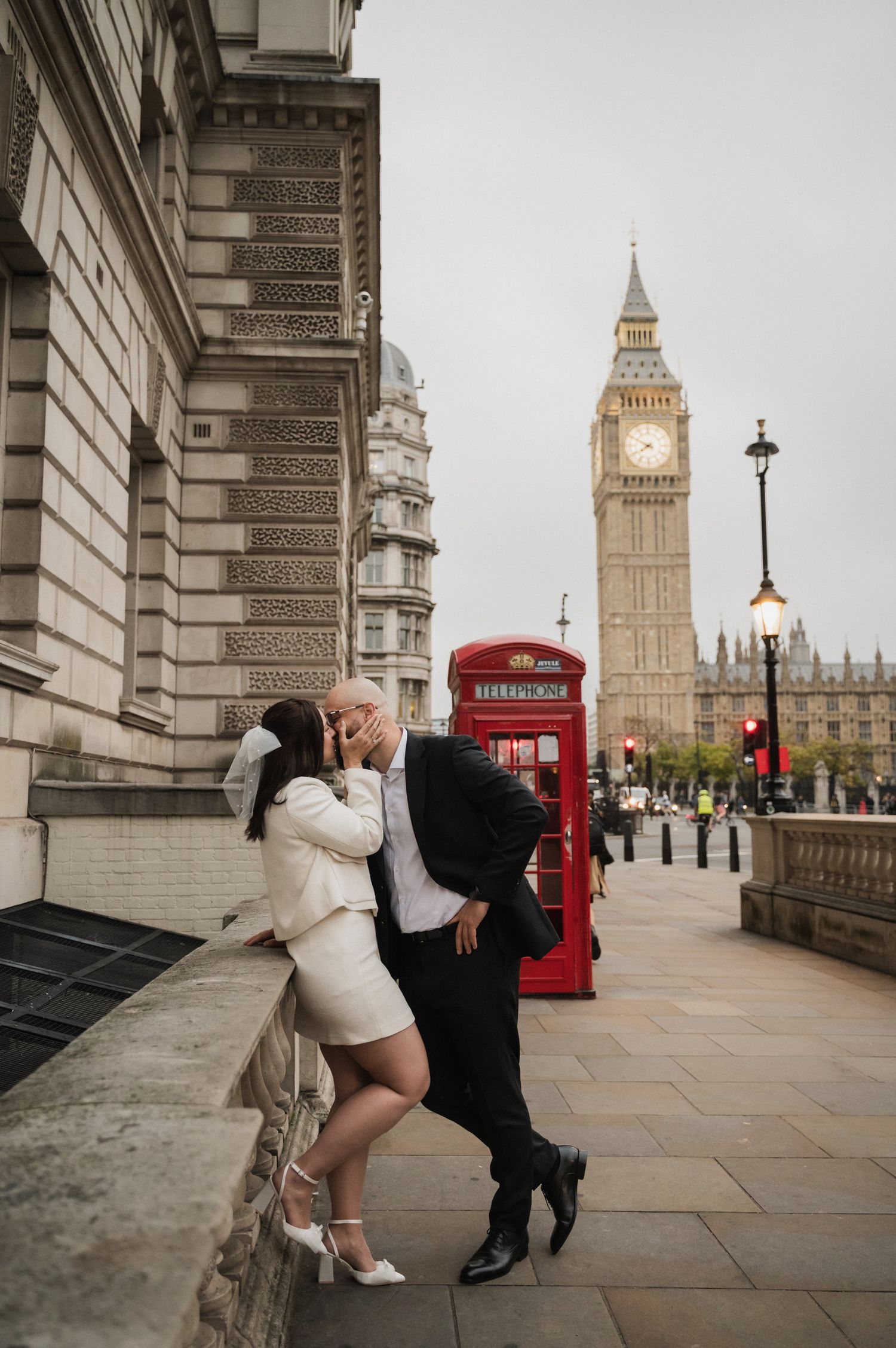 A couple poses playfully near Big Ben and a red phone booth in London.
