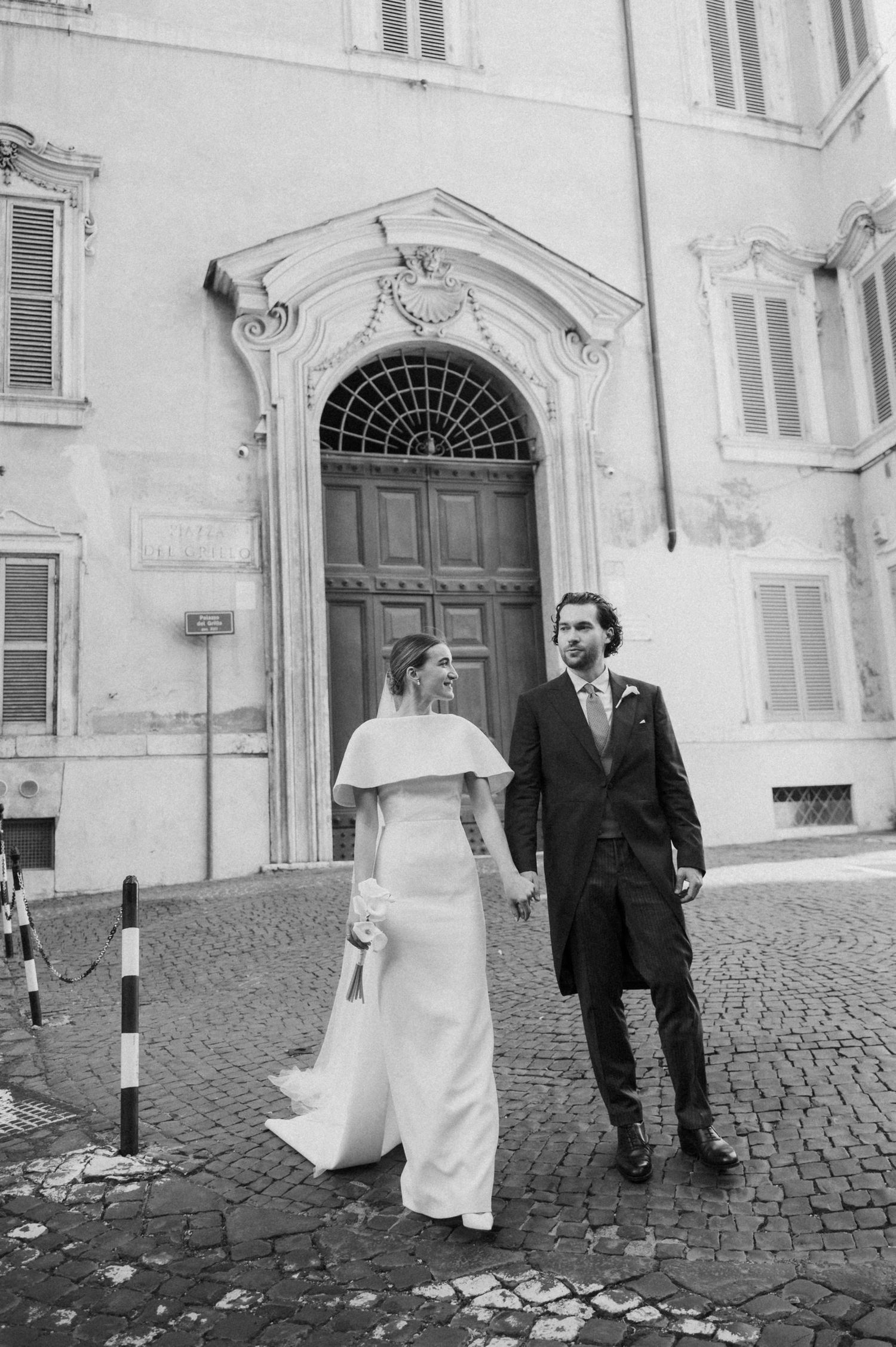 Vintage-style wedding photo on cobblestone street with classic European architecture.