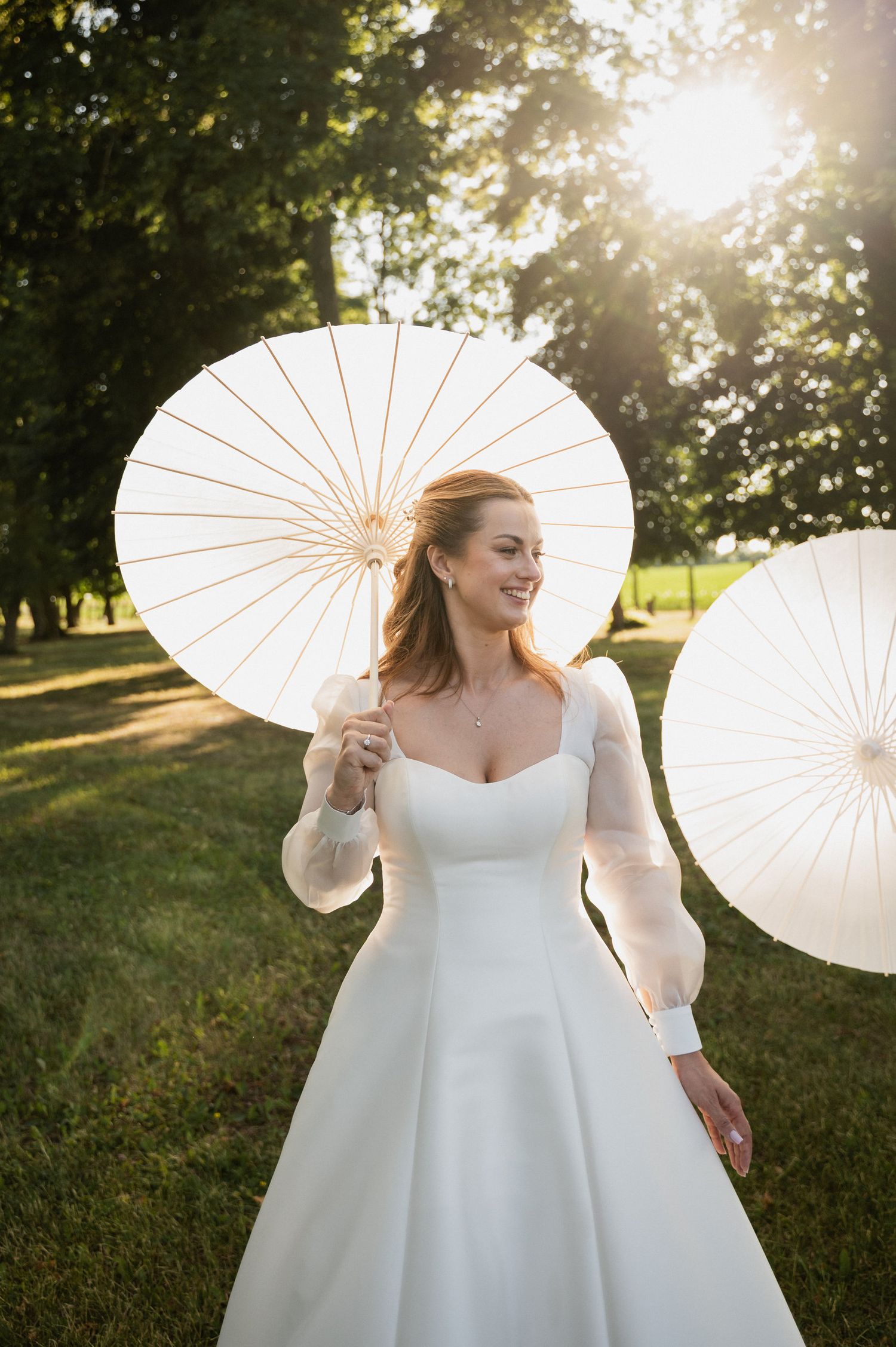 A joyful moment captured in golden sunlight as someone twirls in a flowing white wedding dress while holding paper parasols.