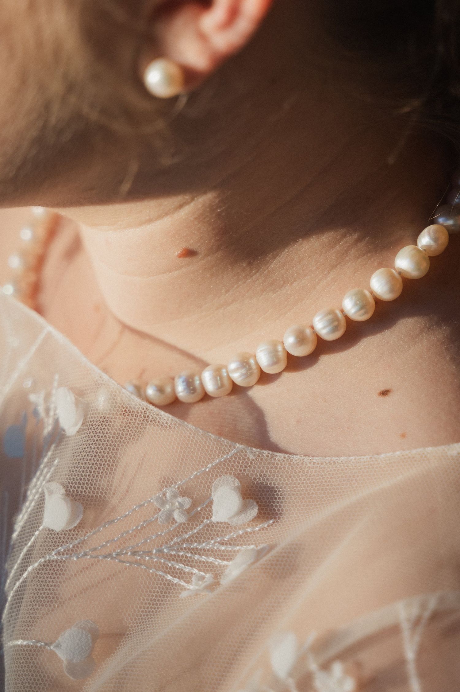 A delicate strand of white pearls rests against sheer tulle fabric in an elegant bridal detail shot.