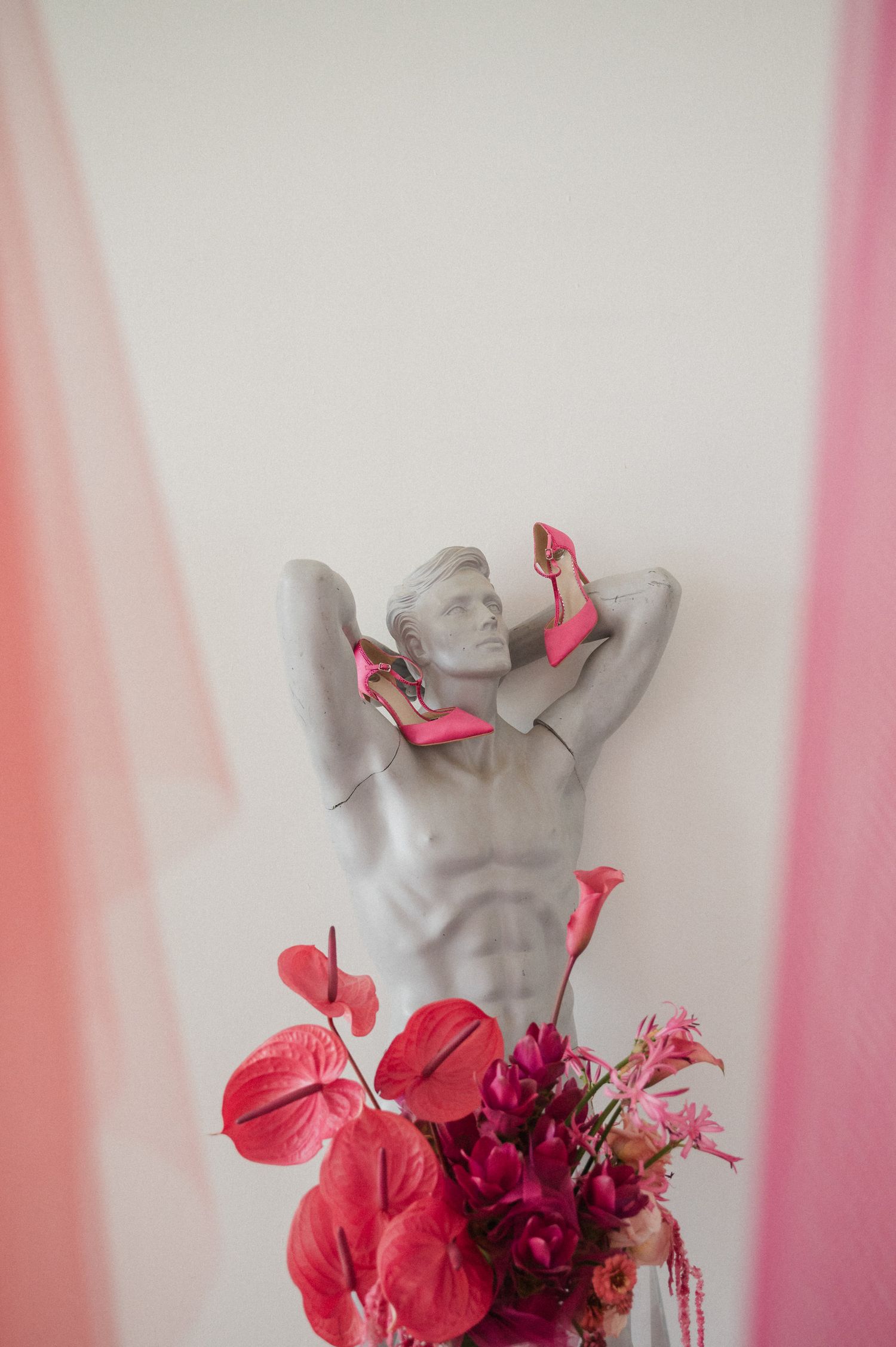 Gray mannequin torso decorated with vibrant pink flowers and anthurium blooms against a light background.
