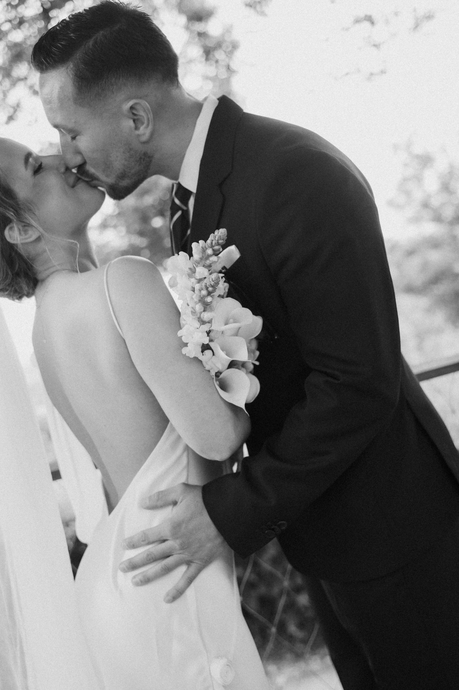Black and white photo of a bride and groom sharing a romantic kiss on their wedding day.