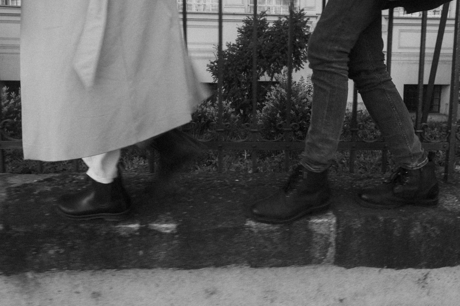 A black and white photo showing several people's legs and feet standing together in a group outdoors.
