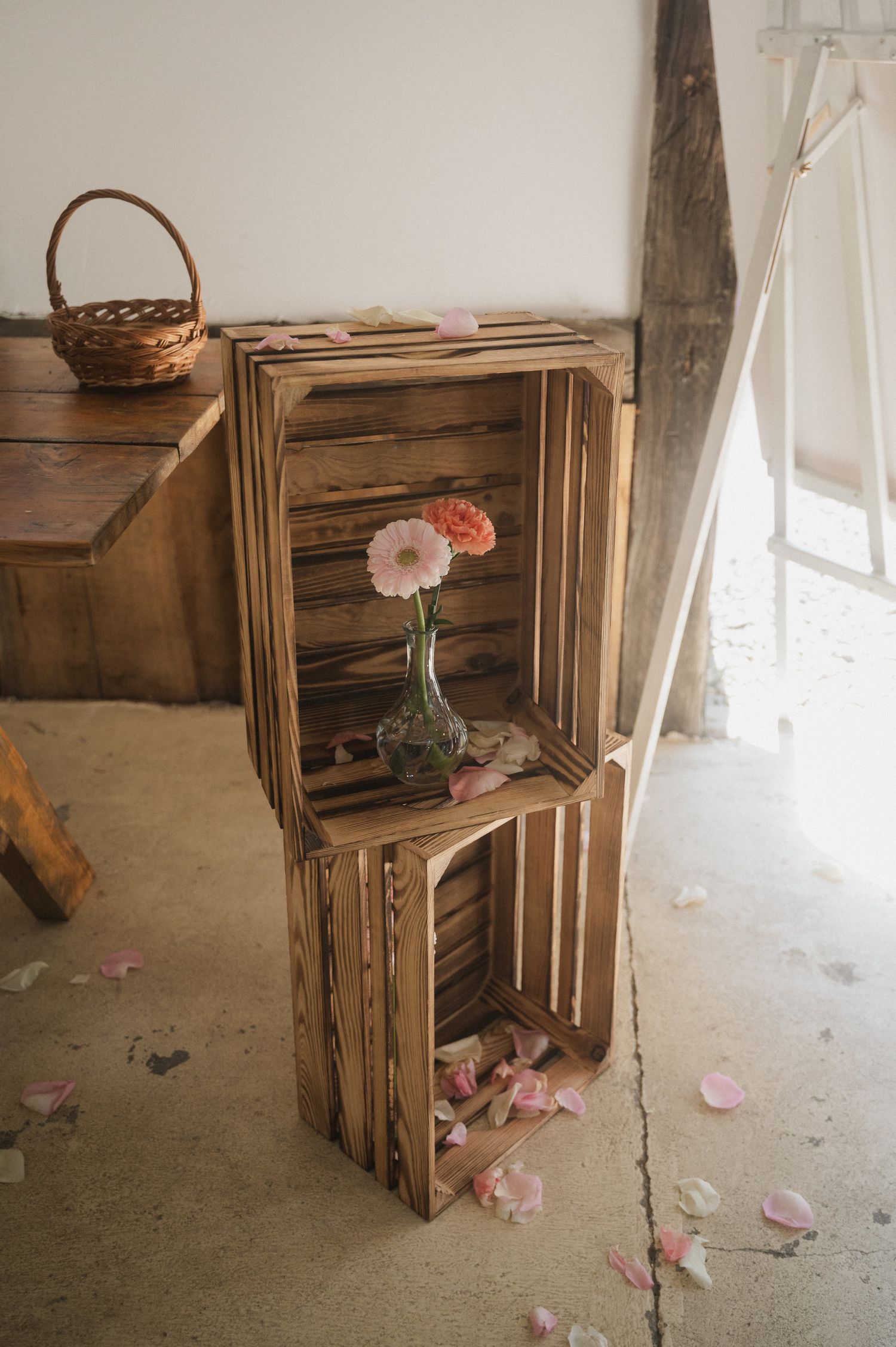 Rustic wooden crates arranged with delicate pink flowers and white curtains in a vintage-style interior setting.