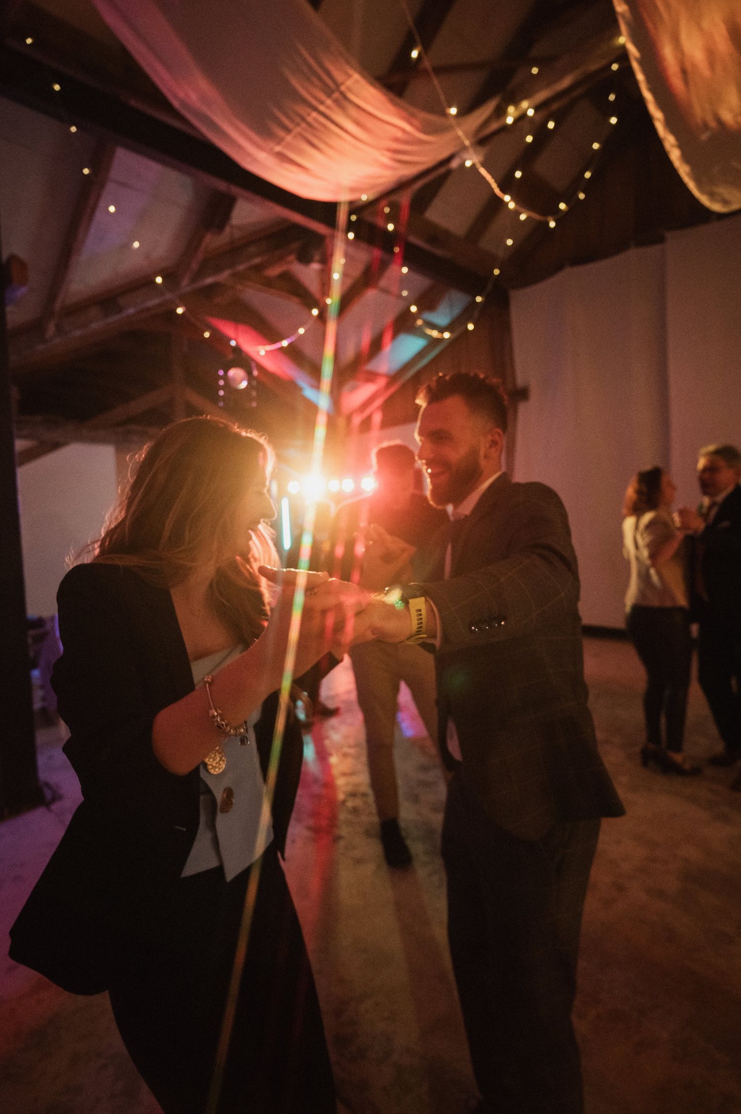 Silhouetted couples dancing at a romantic reception with fairy lights and fabric draping overhead.