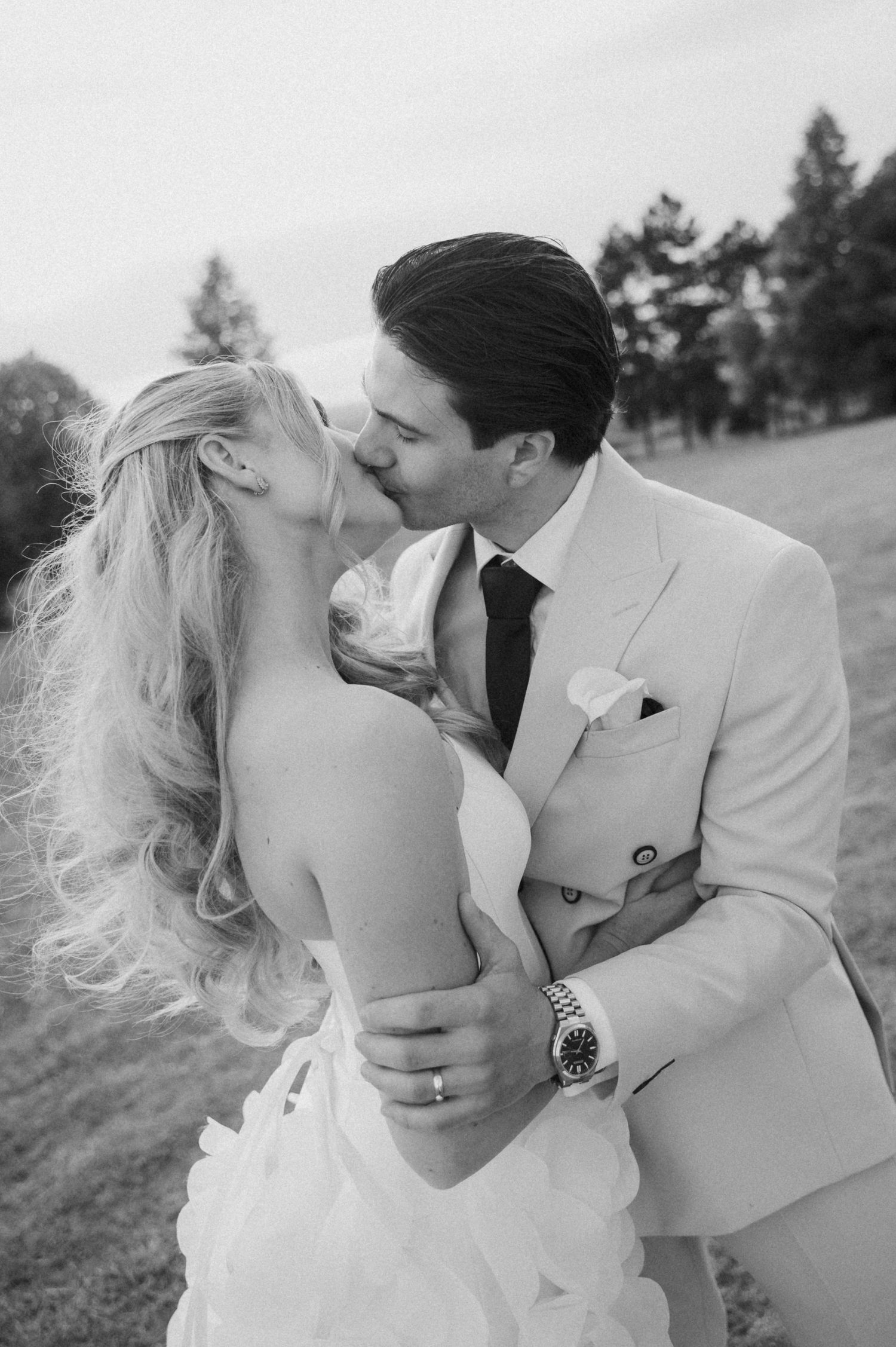 Bride and groom sharing a romantic kiss outdoors in a black and white wedding portrait.