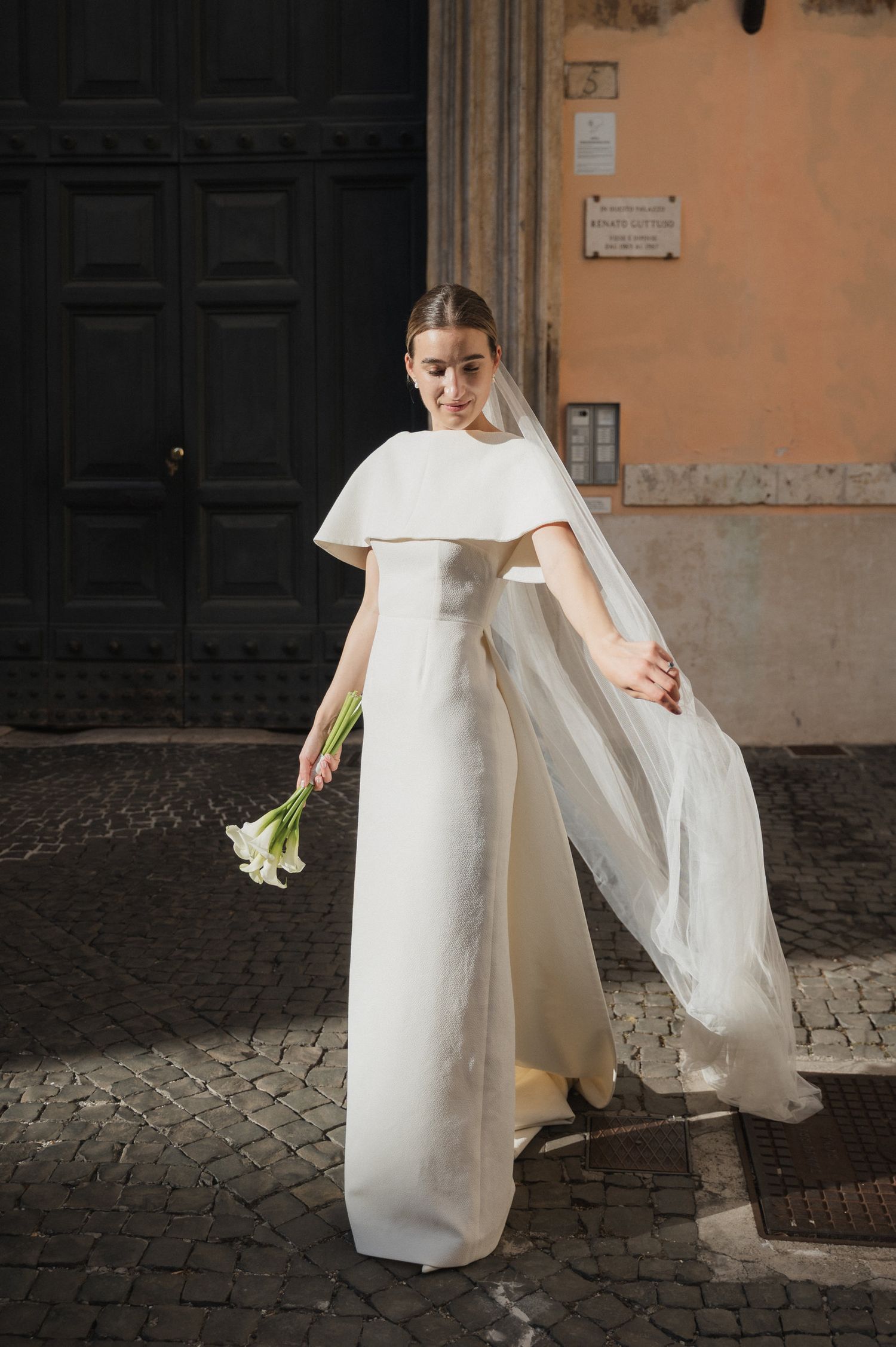 Bride in minimalist white dress walking on historic cobblestone street.